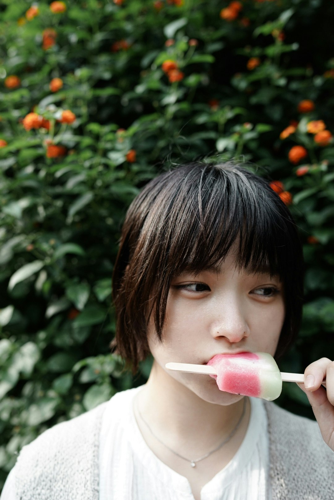 꽃이 핀 덤불 앞에서 아이스크림을 먹는 여성
