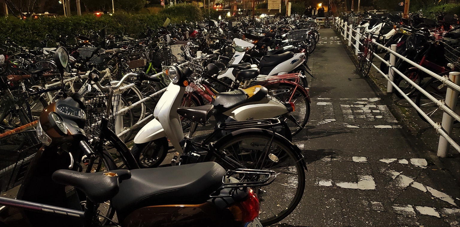 Un área de estacionamiento de motocicletas llena por la noche con varias motos y bicicletas