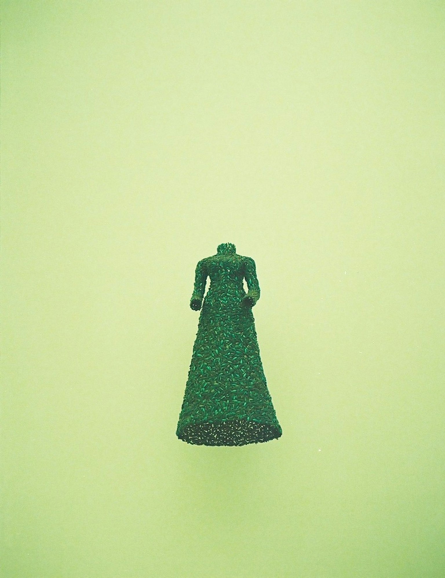 Une figurine de robe verte se dresse sur un fond vert clair