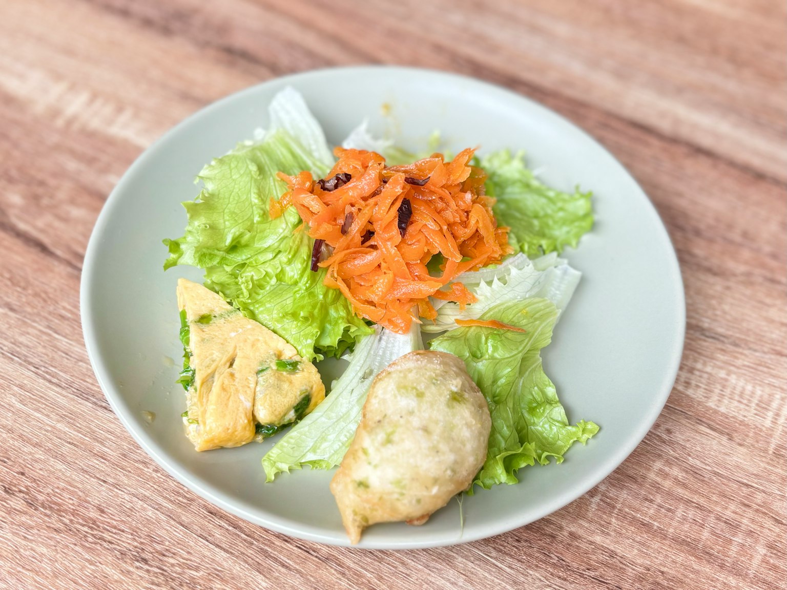 Un plato con lechuga verde y ensalada de zanahorias, que incluye una tortilla y comida frita