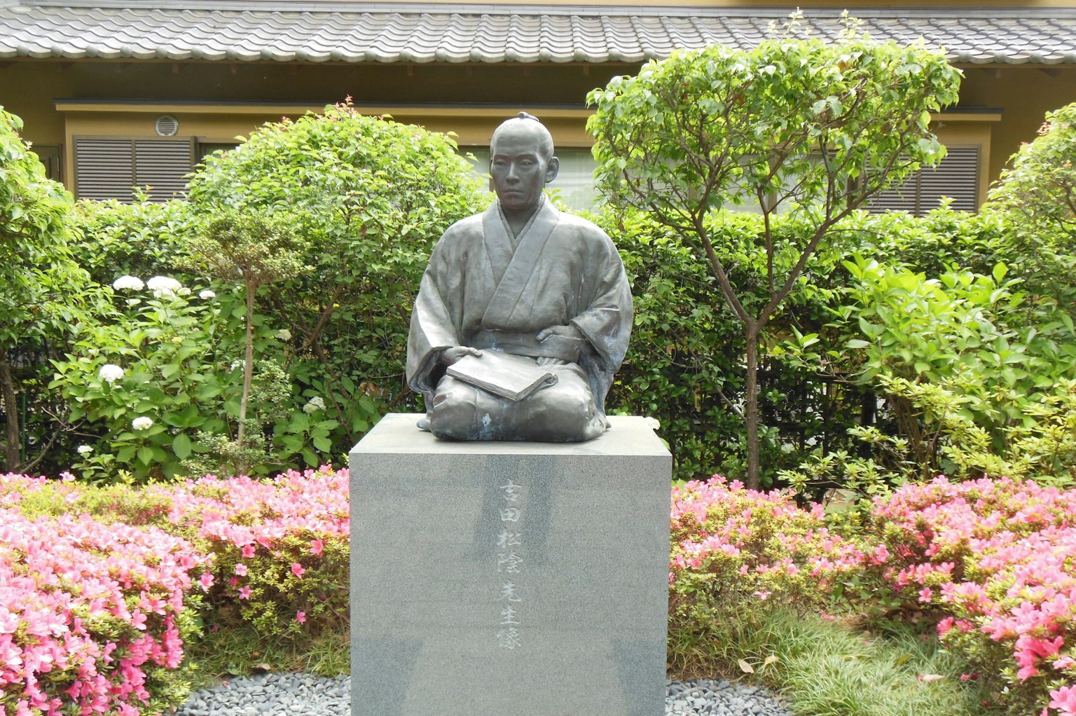 Bronze statue seated in a garden surrounded by colorful flowers