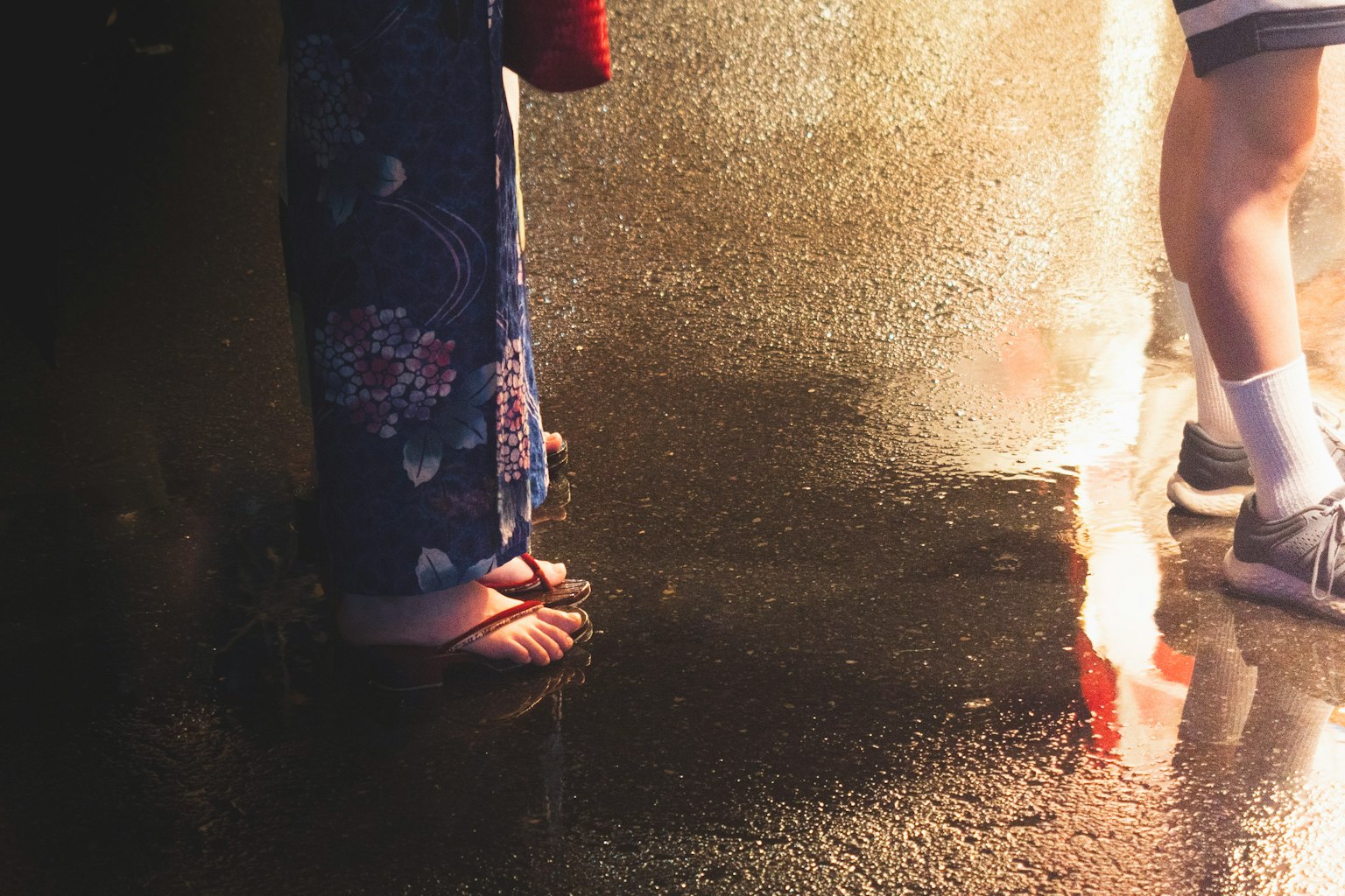 Dua pasang kaki berdiri di permukaan basah satu mengenakan yukata tradisional dan yang lain berpakaian kasual