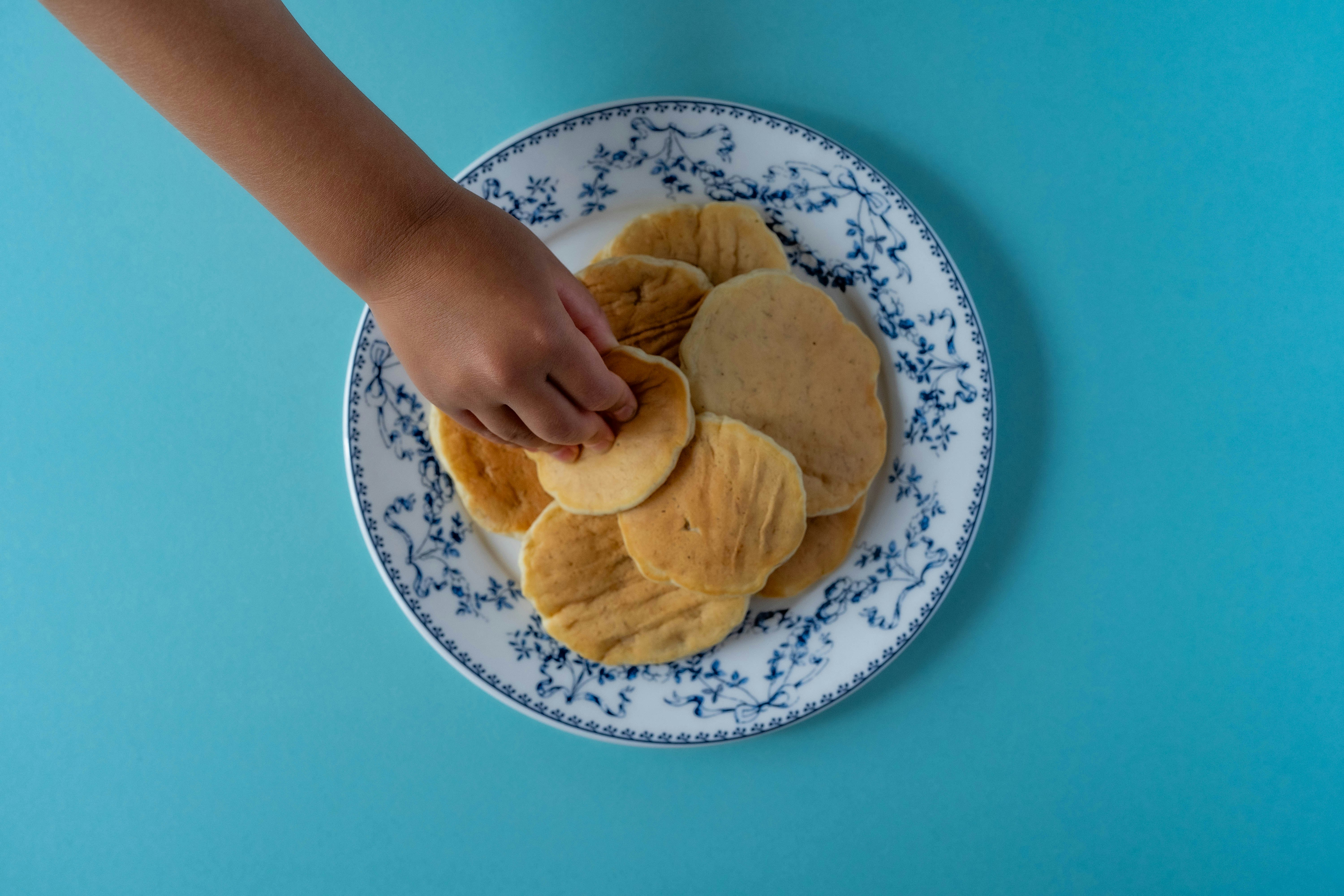 Tangan meletakkan pancake di atas piring dengan latar belakang biru