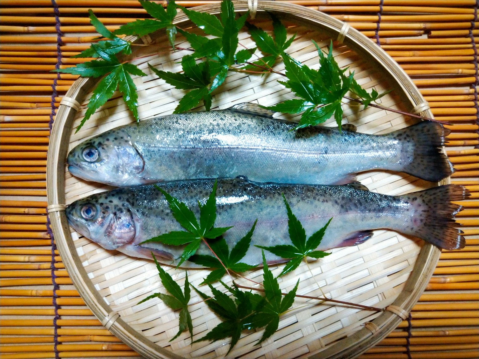 Deux poissons avec des feuilles vertes disposées sur une assiette en bambou