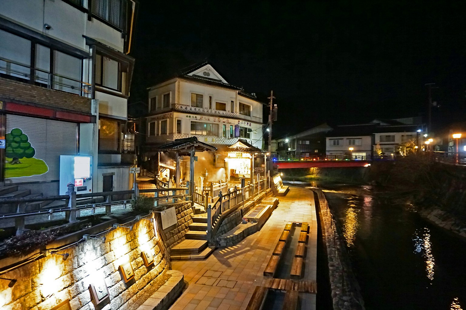 Pemandangan malam kota pemandian air panas dengan bangunan yang diterangi dan sungai yang indah