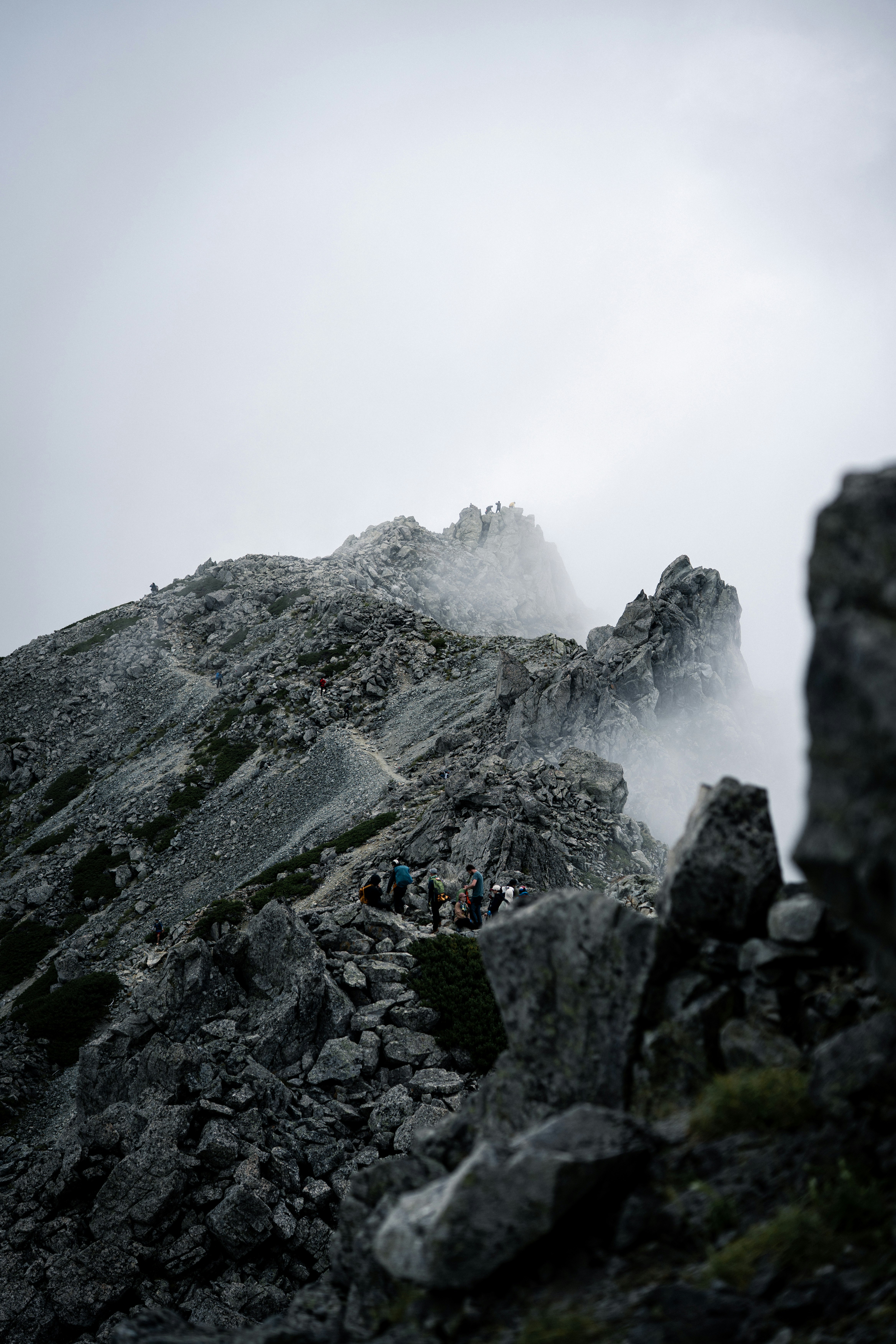 岩稜と霧のかかった山道を歩く登山者たち
