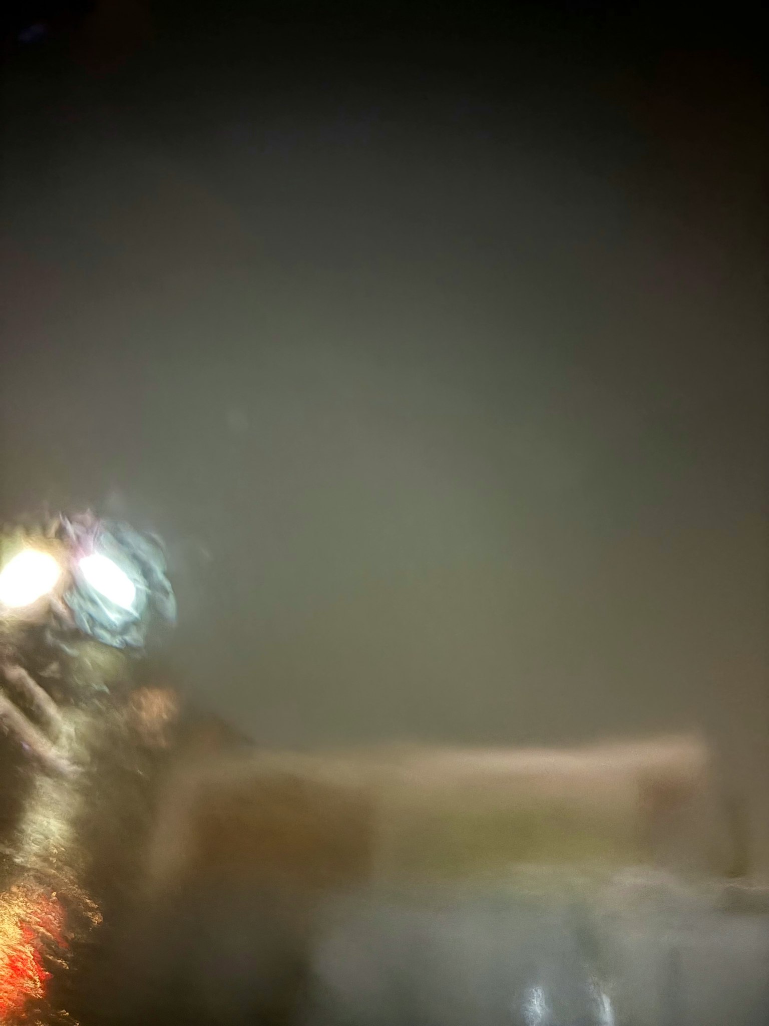 ぼやけた夜の風景に光る車のヘッドライトと水たまりが映る
