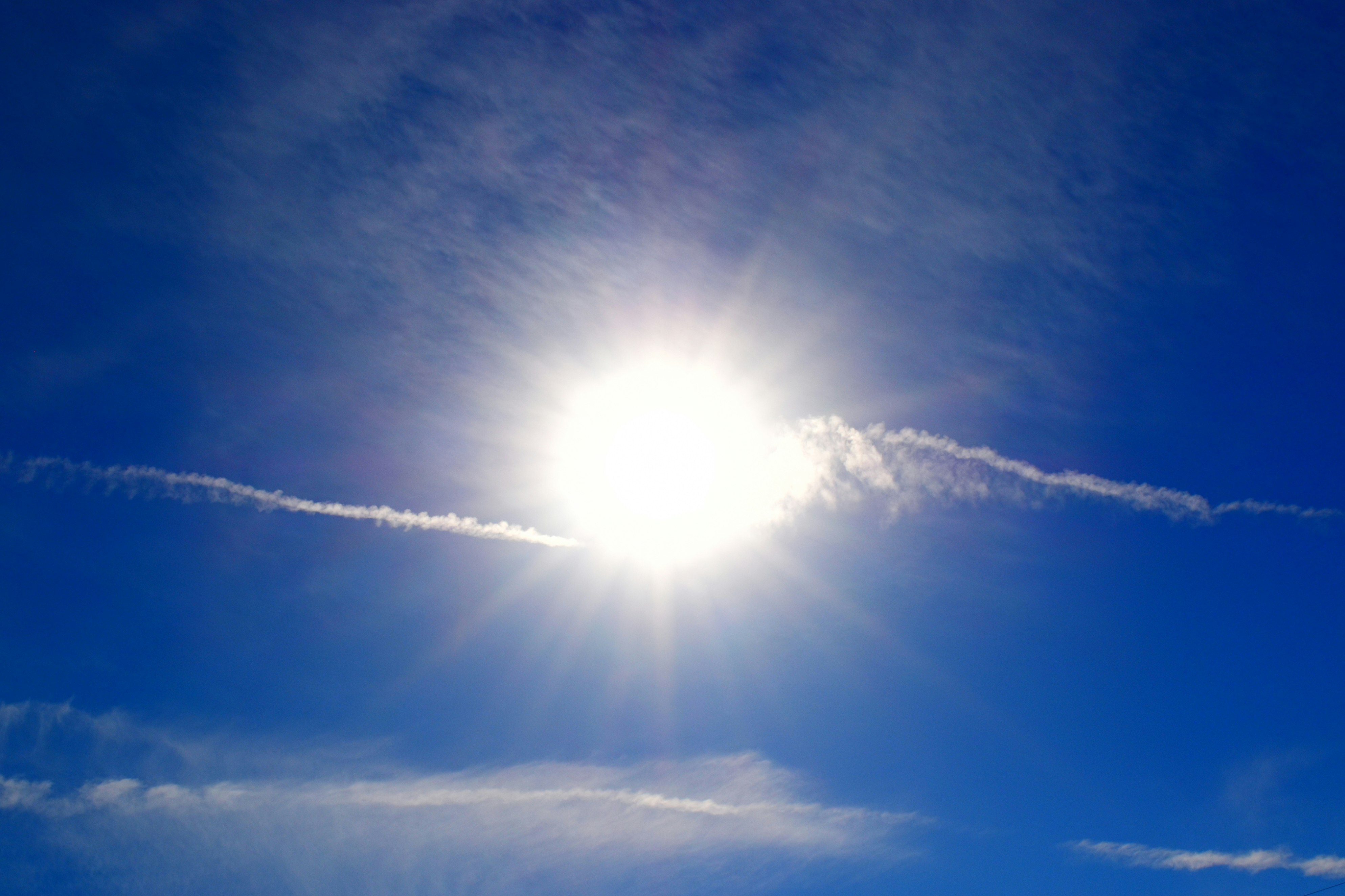 筋雲の広がる青空に太陽が輝く空