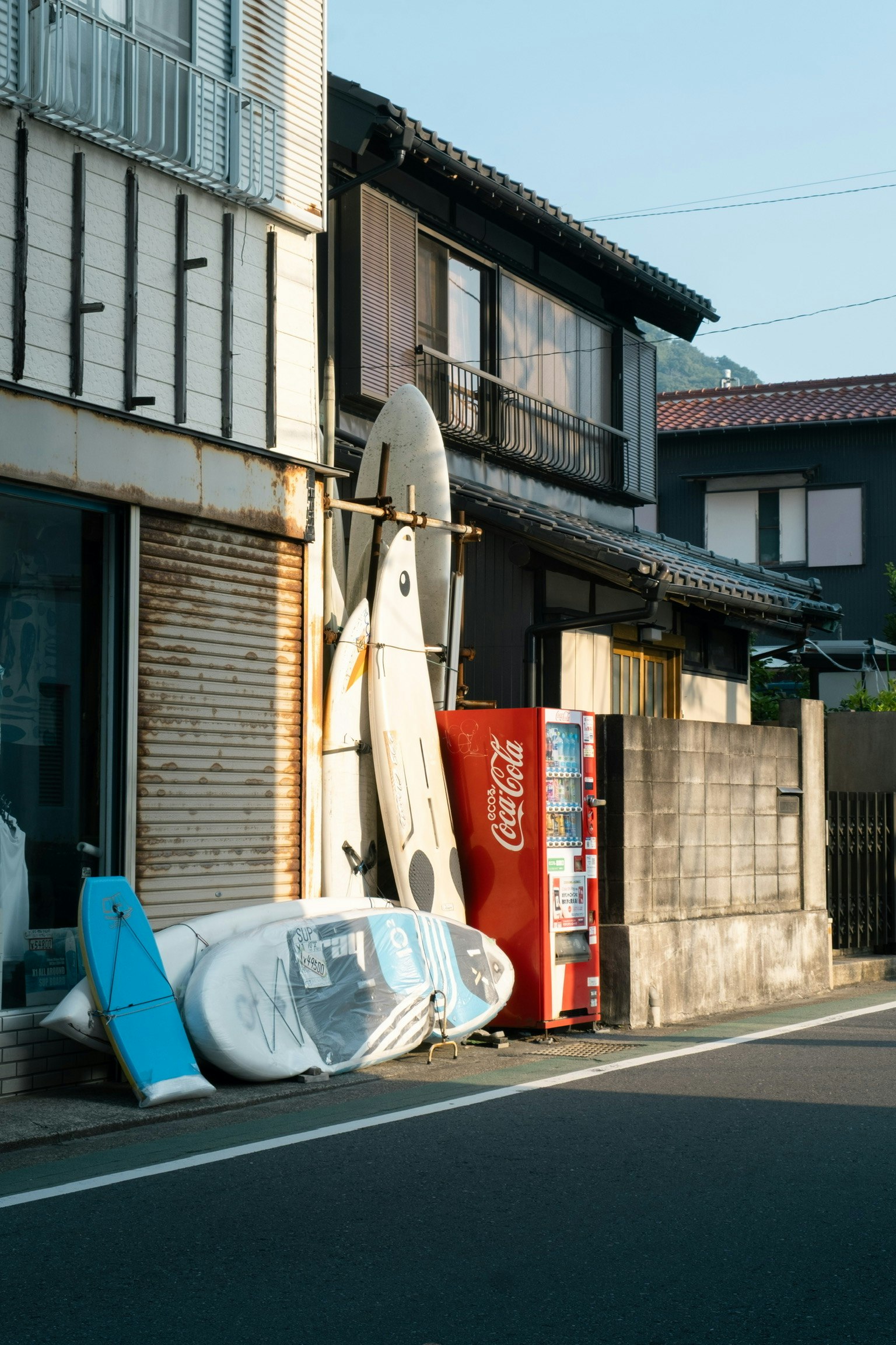 夏の通り道に置かれた自販機とサーフボードのある路地