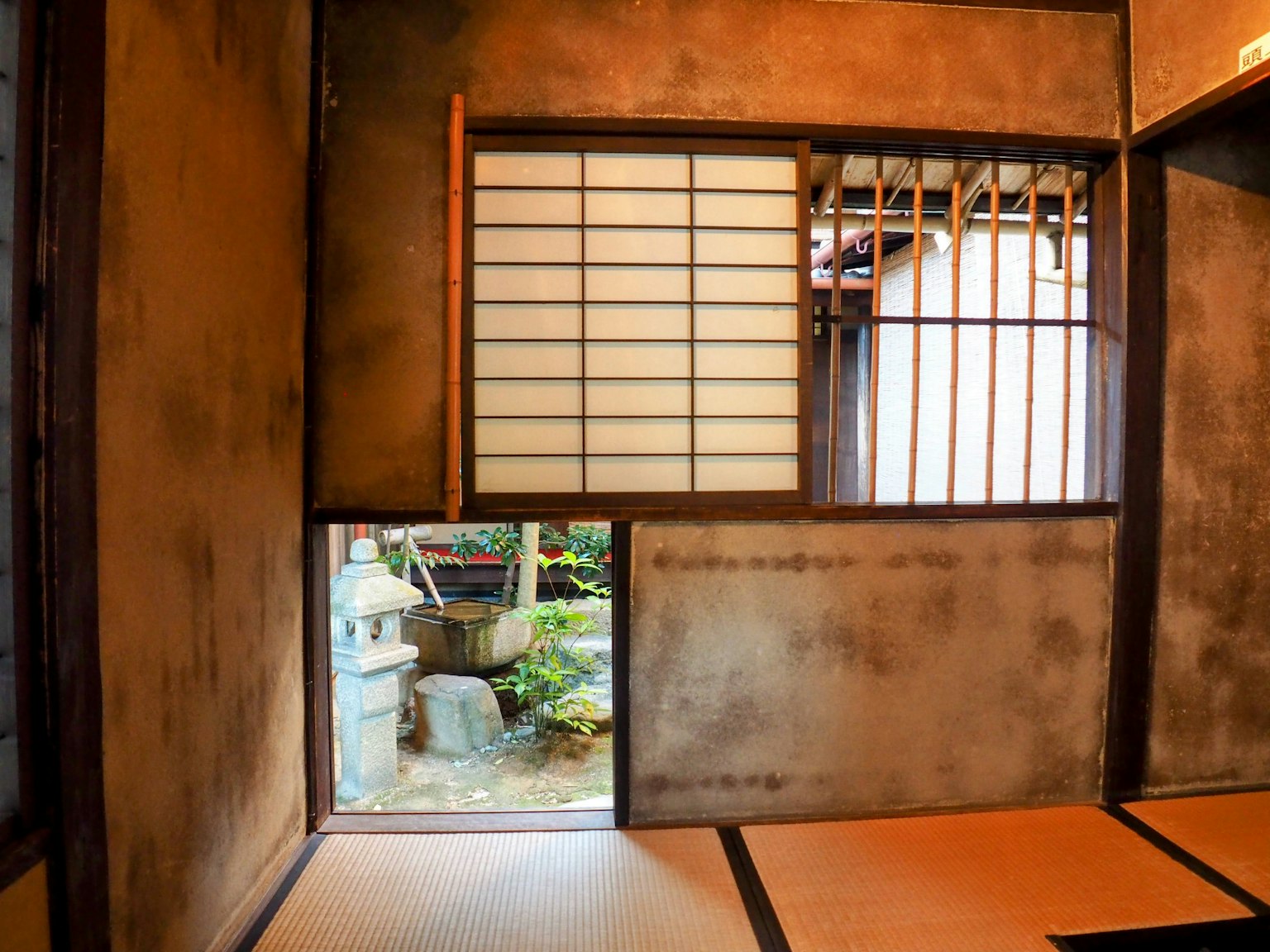 Vista interna di una stanza giapponese tradizionale che si affaccia su un giardino con muri in terra e pavimento in tatami