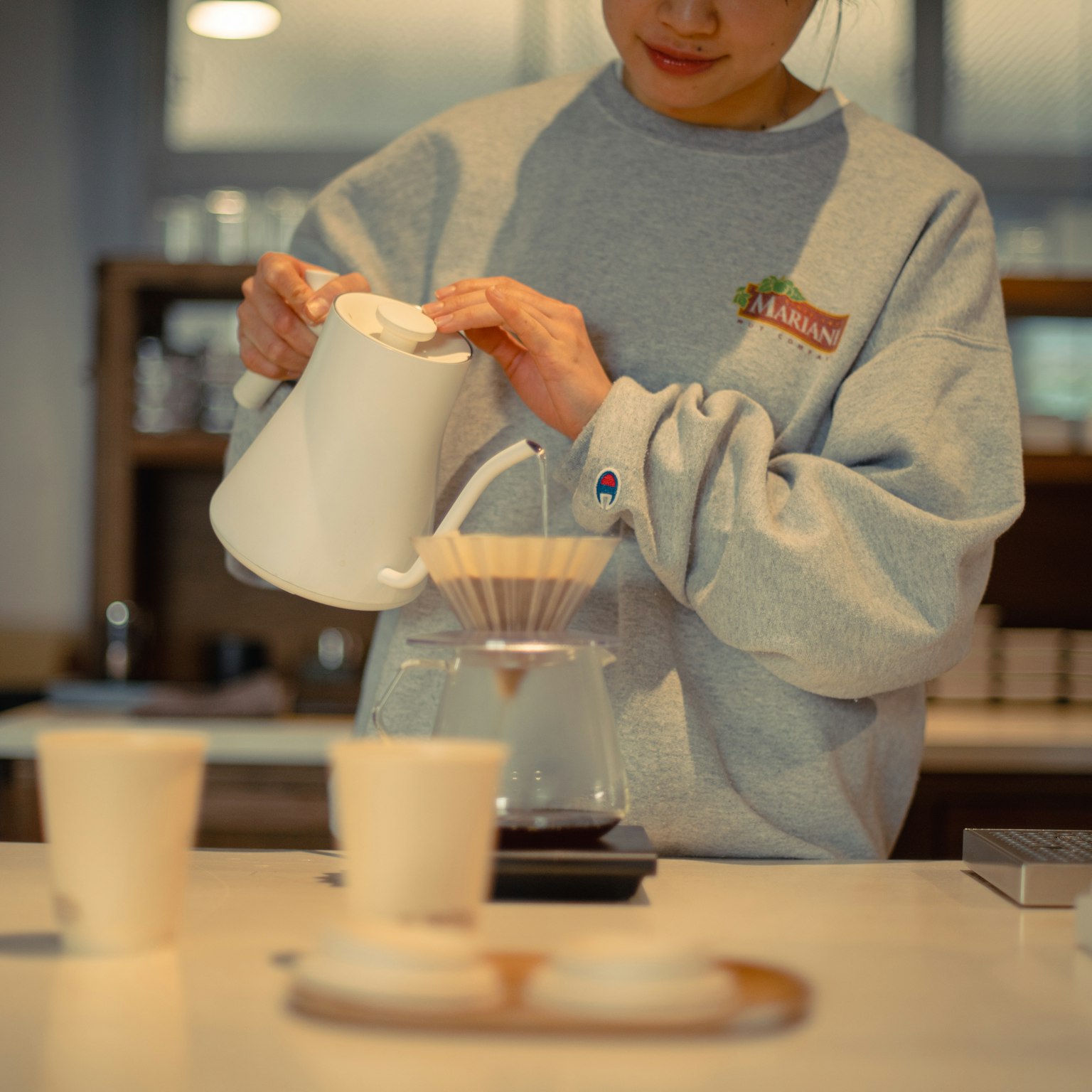 Một người phụ nữ đang rót cà phê bằng ấm vào bộ lọc