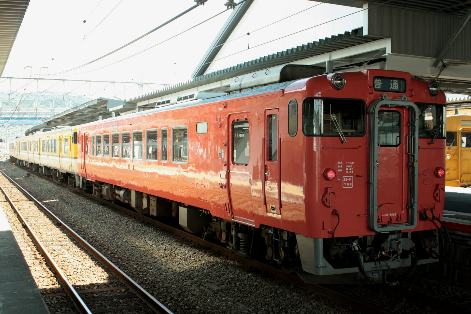 Sebuah kereta merah berhenti di stasiun dengan kereta dan platform lain terlihat di latar belakang