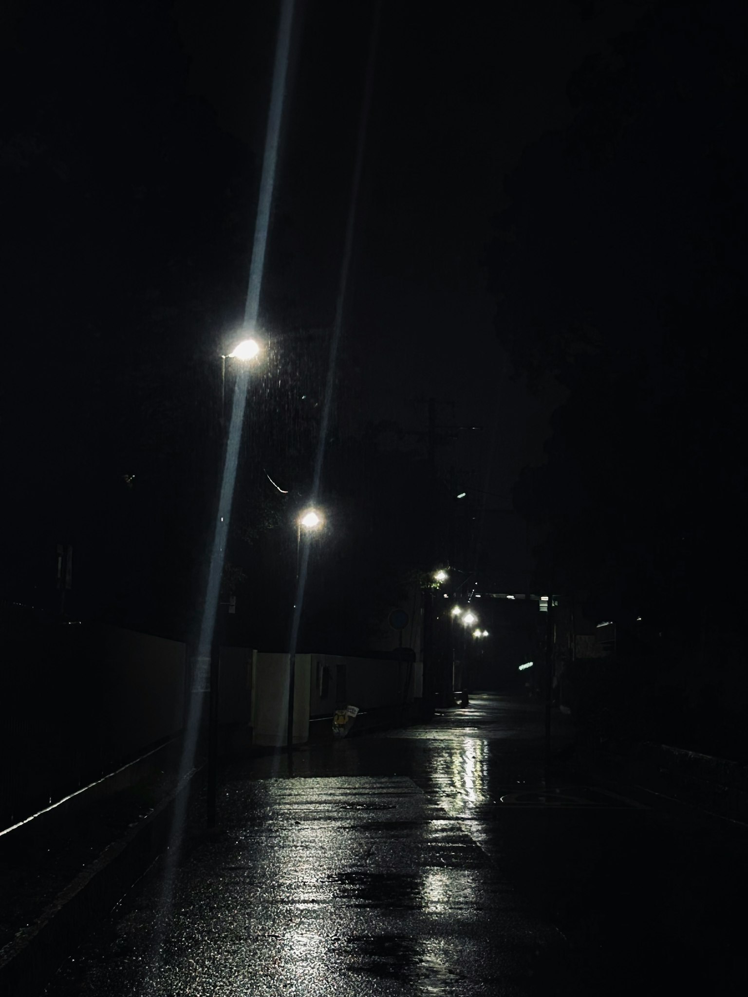 A dark street illuminated by streetlights with wet pavement