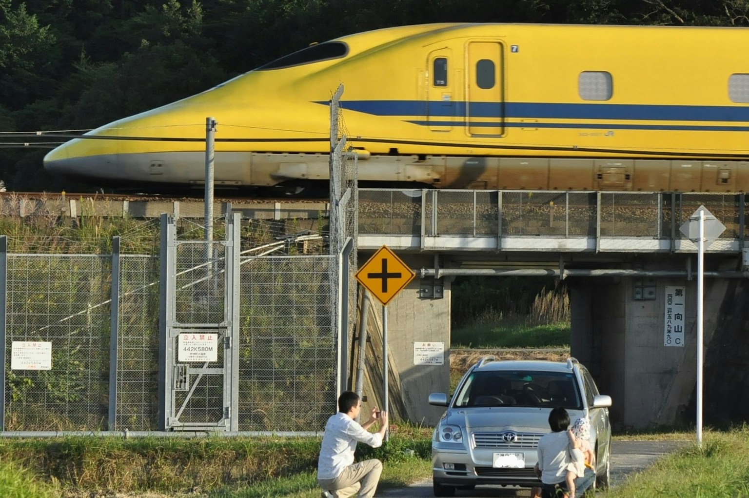 รถไฟชินคันเซนสีเหลืองวิ่งผ่านถนนที่มีรถยนต์ด้านล่าง