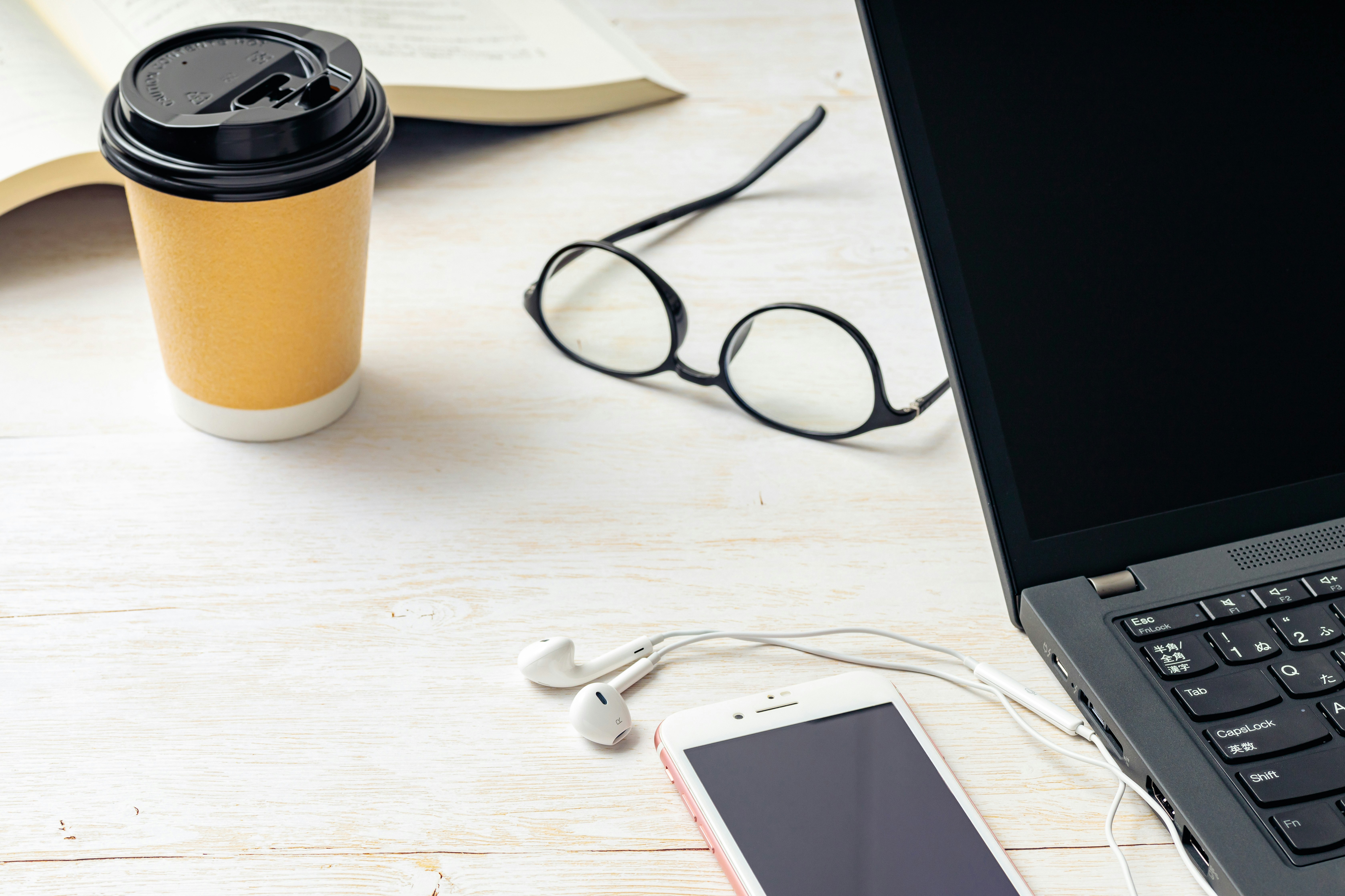 ビジネス机上のコーヒーとPC、スマホ、メガネ、イヤホン