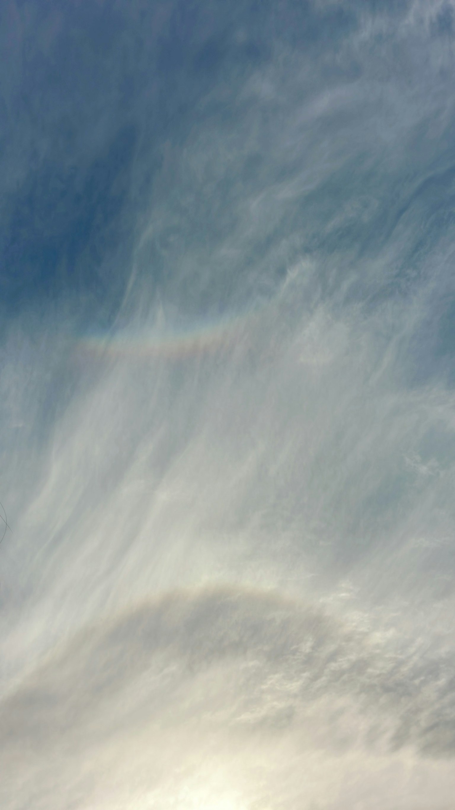 Wolken mit einem schwachen Regenbogen im blauen Himmel