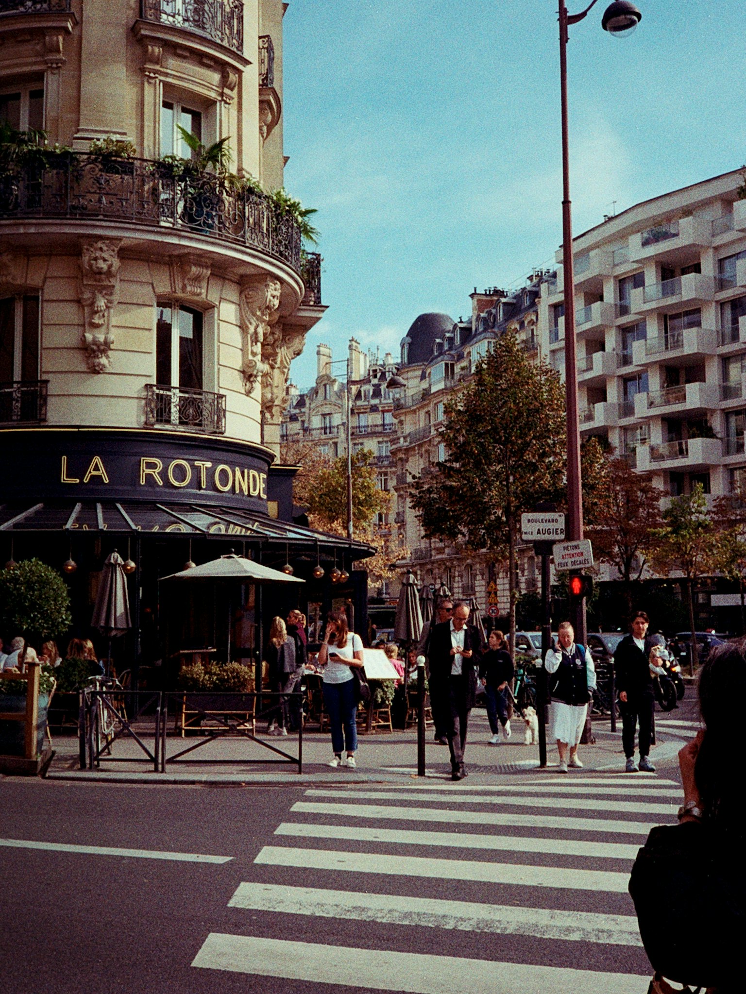 パリの交差点で人々が横断歩道を渡る様子 カフェのテラスと建物が見える