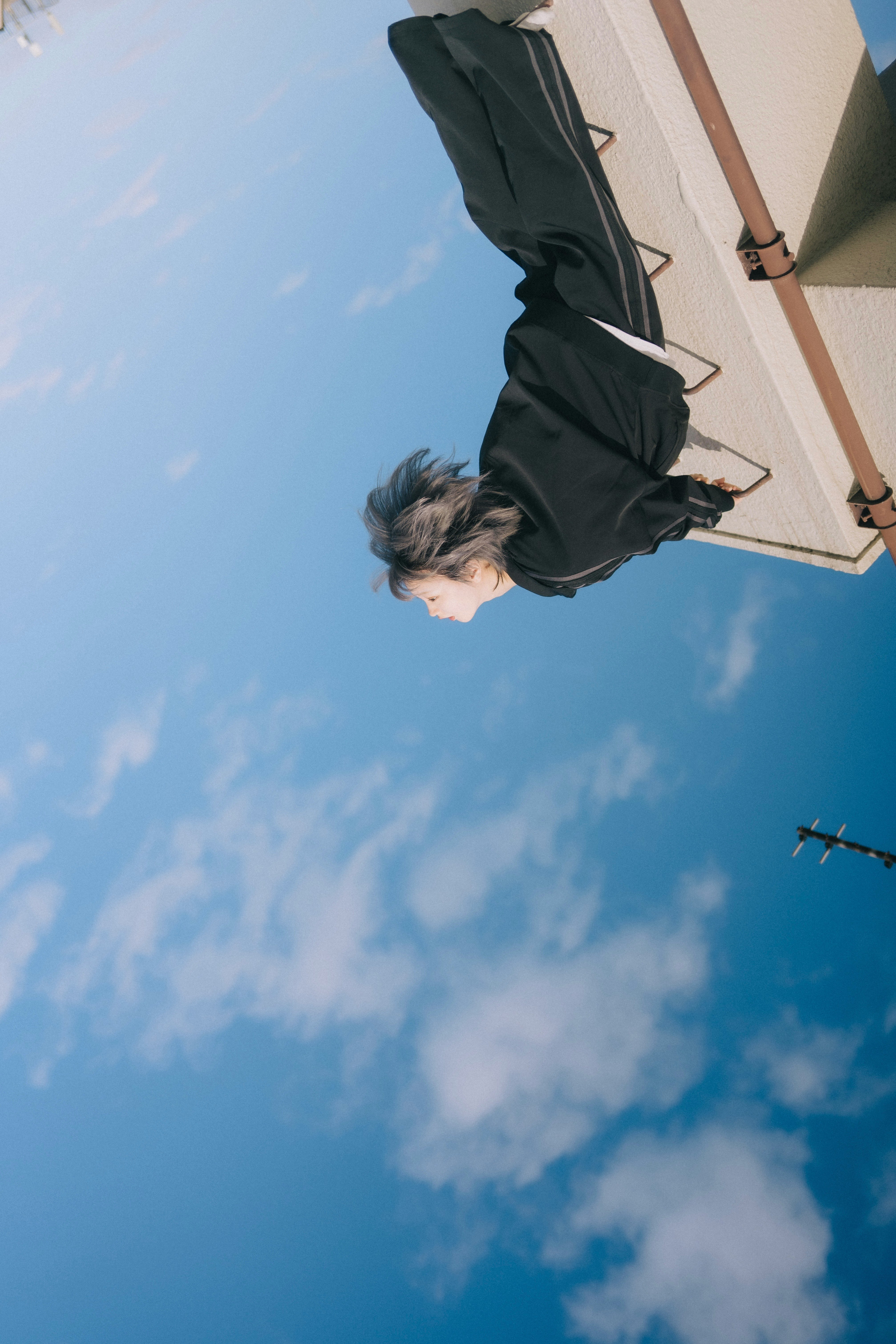 青空の下で風に揺れる黒いコートの人物