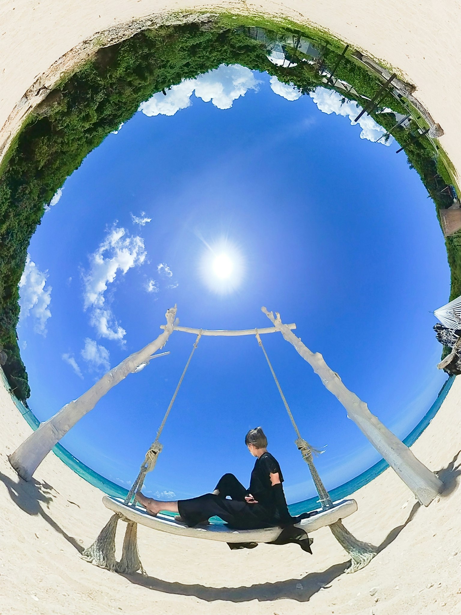 Eine Person sitzt auf einer Schaukel mit blauem Himmel und weißem Sandstrand
