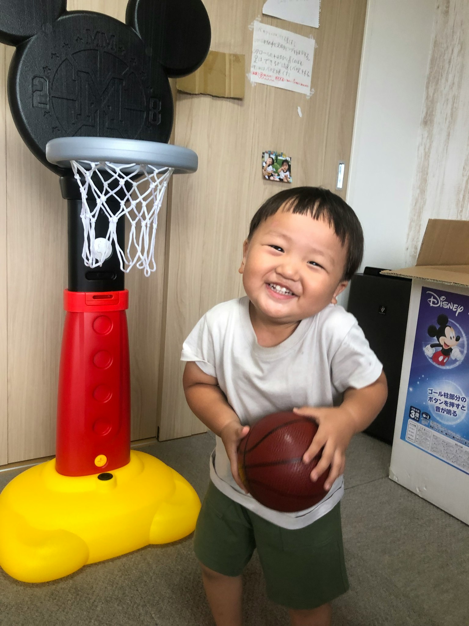 Lächelndes Kind mit einem Basketball vor einem Mickey Mouse Basketballkorb