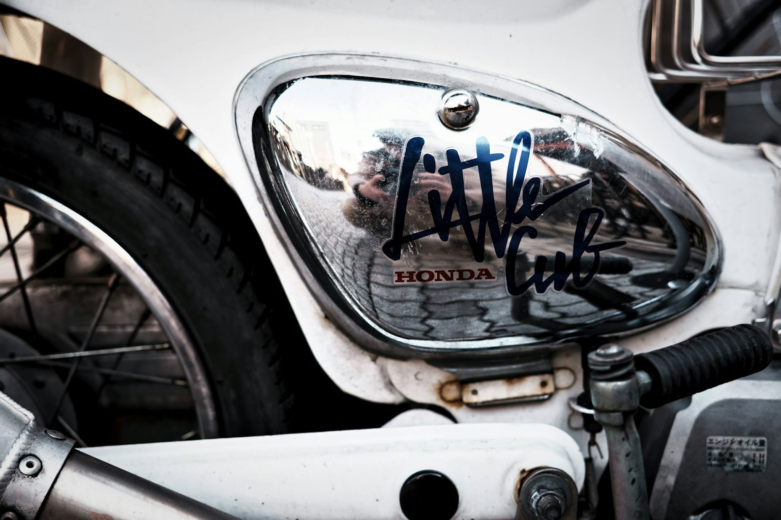 흰색 오토바이의 근접 사진으로, 반사된 주변과 그래피티가 있는 탱크