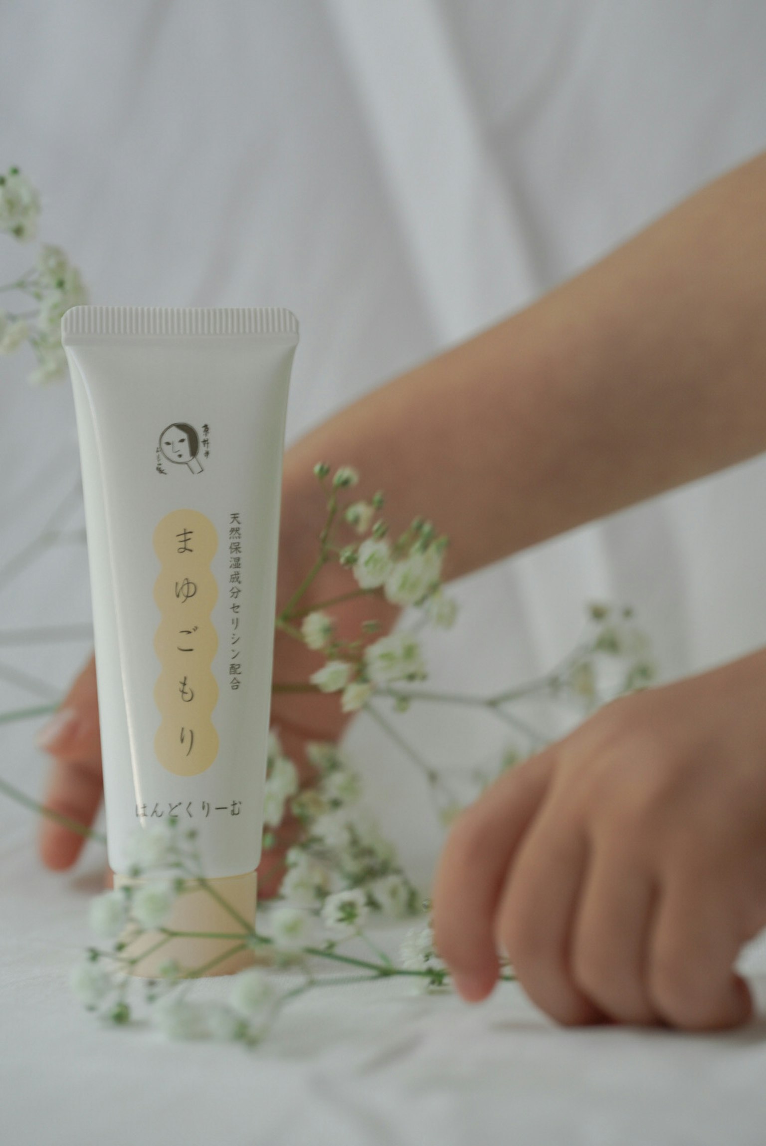 一只手在白色背景上拿着小花和化妆品管