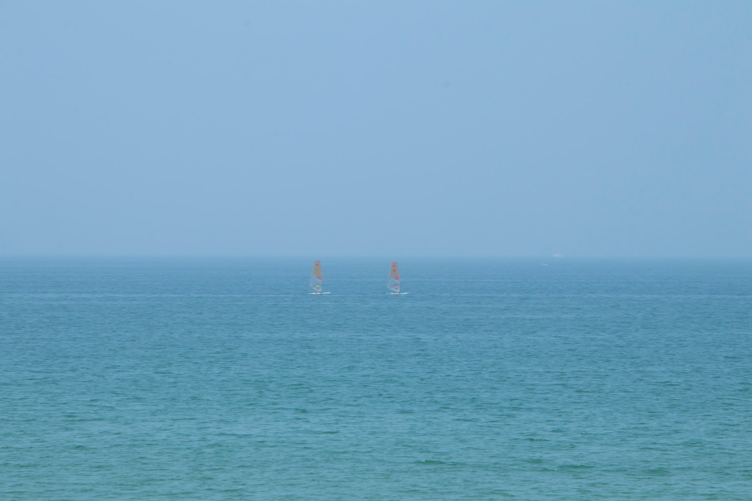 Two sailboats in the distance on a blue sea with a hazy sky