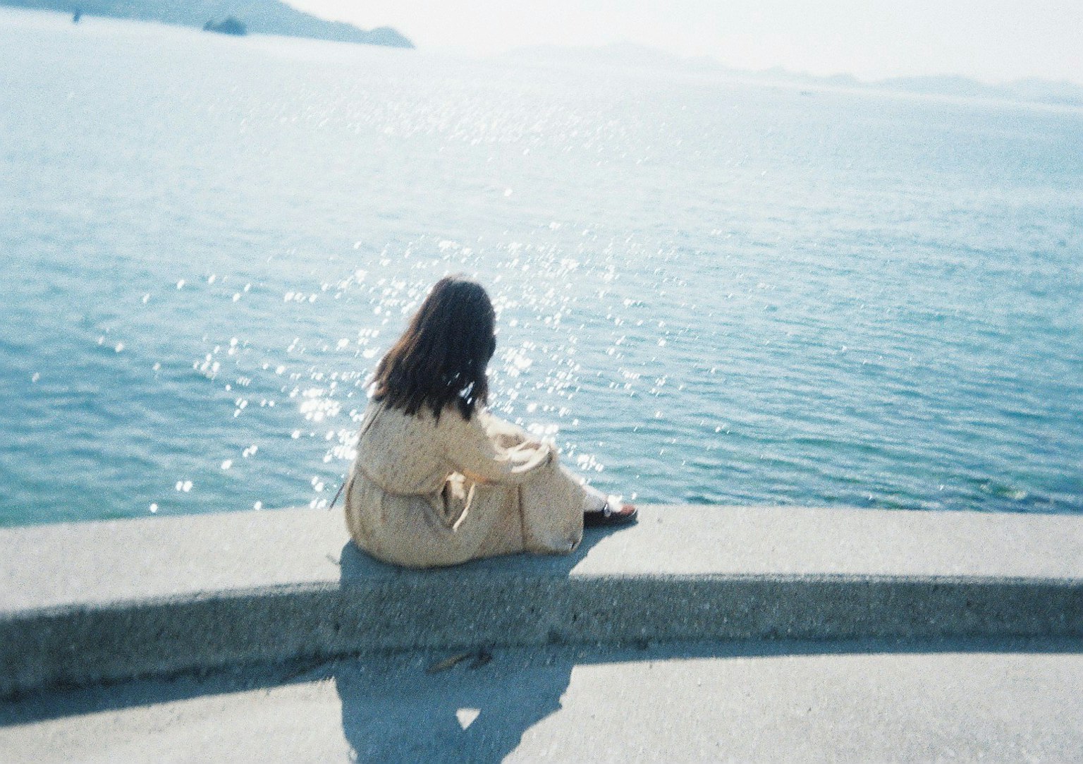 一位女性背对镜头坐在海边