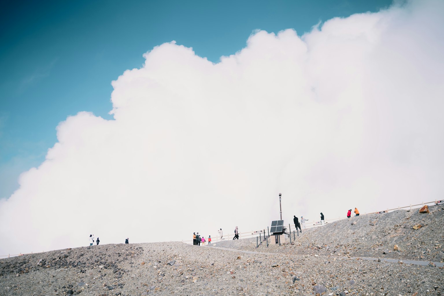 Menschen stehen auf einem Berggipfel umgeben von Wolken und blauem Himmel