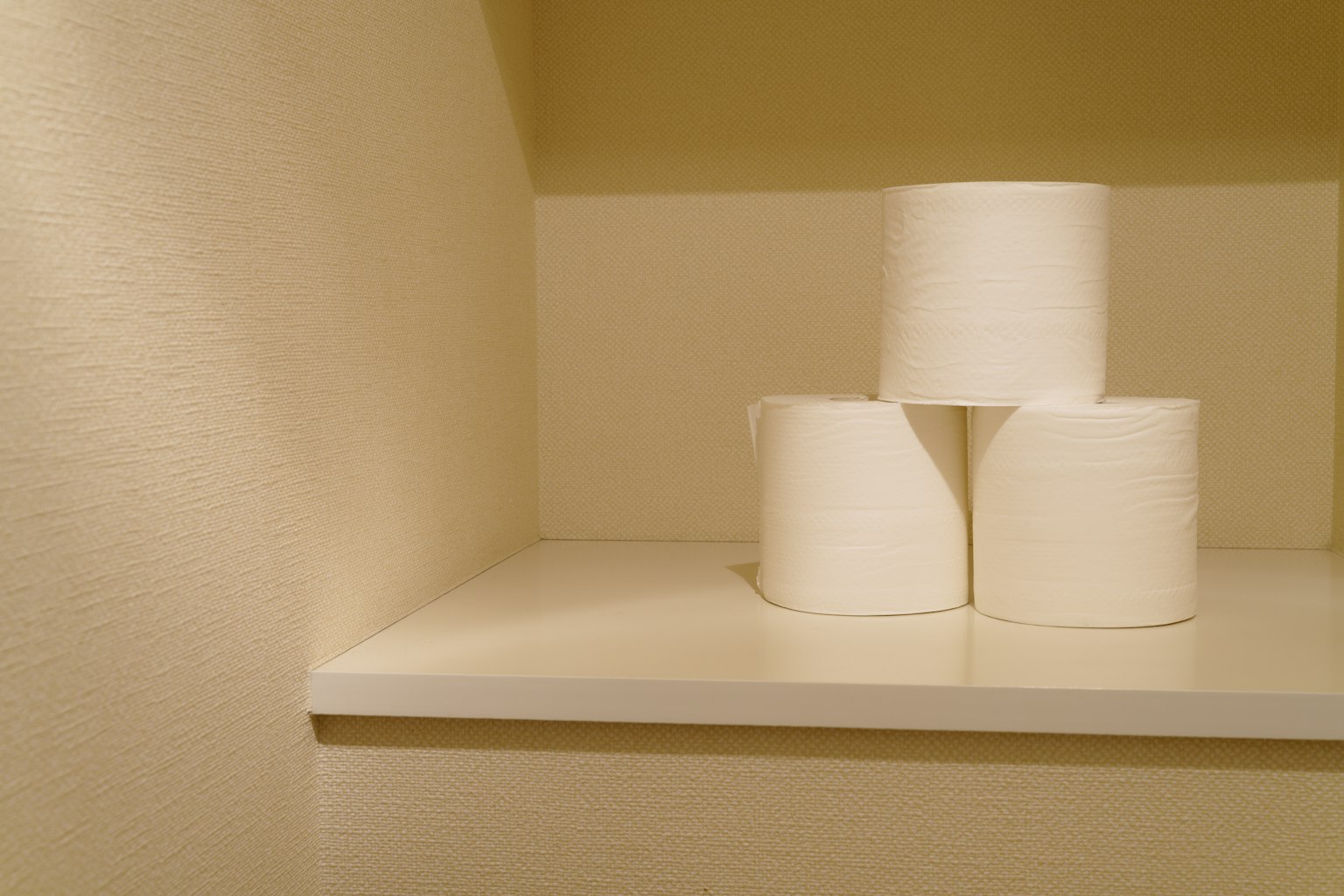 Tiga gulungan kertas toilet putih ditumpuk di sudut rak