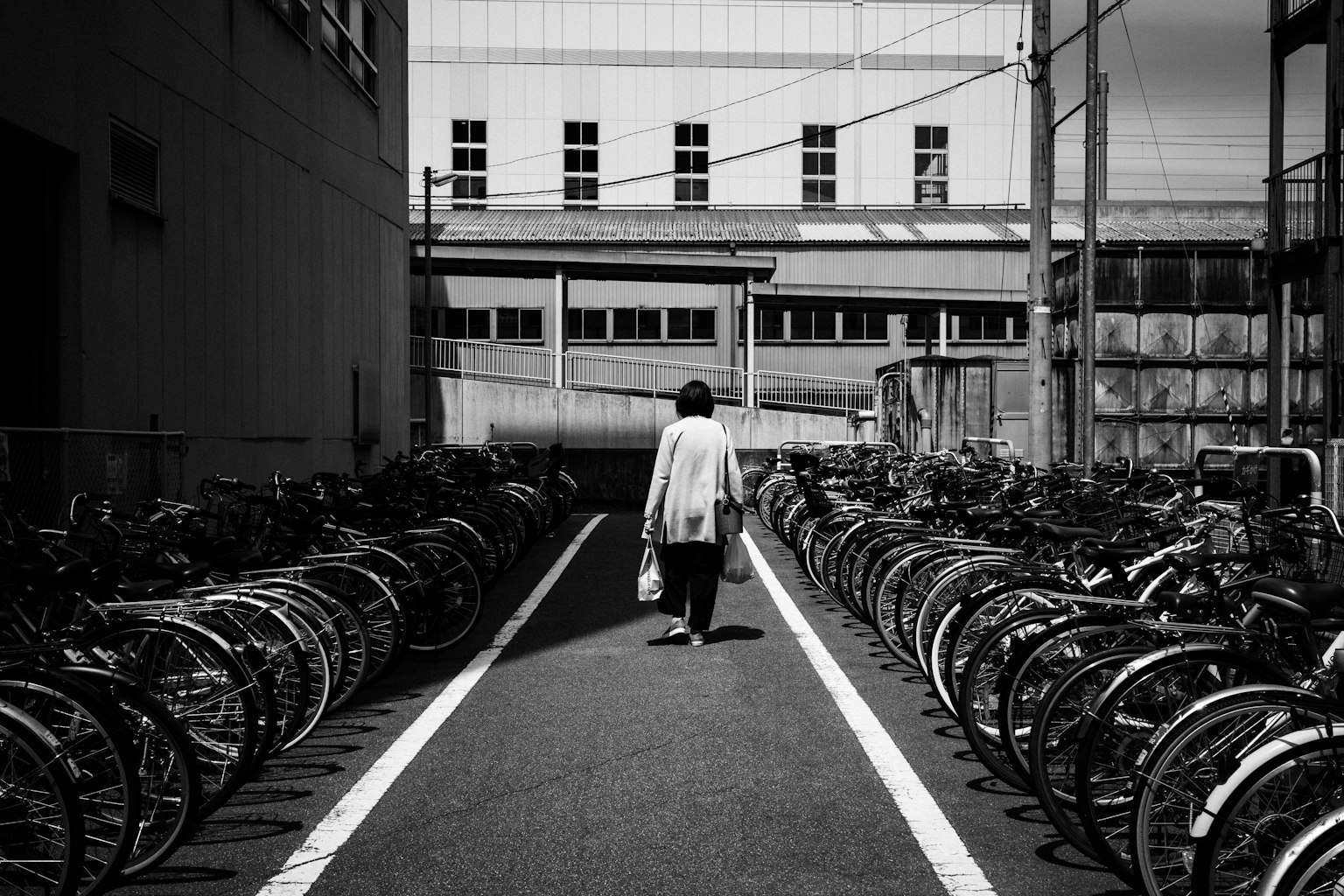 Foto en blanco y negro de una persona caminando por un camino flanqueado por bicicletas