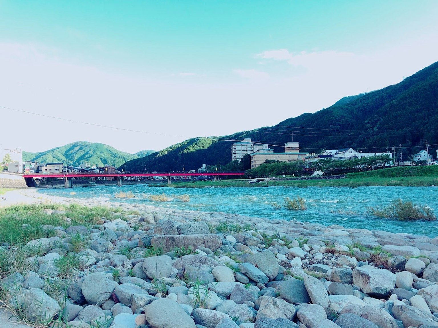 蓝色河流与岩石岸边的风景，红色桥梁与山景相映