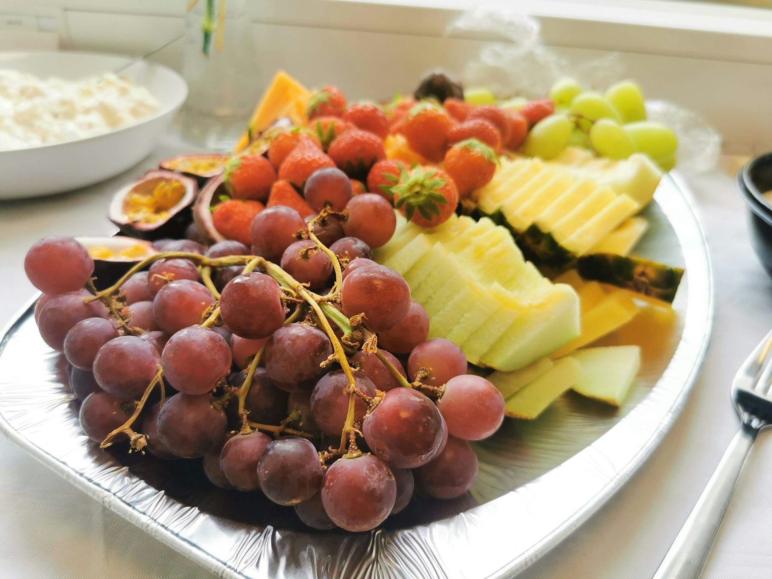 Ein Teller mit verschiedenen Früchten einschließlich roter Trauben, Melone, Ananas und grünen Trauben