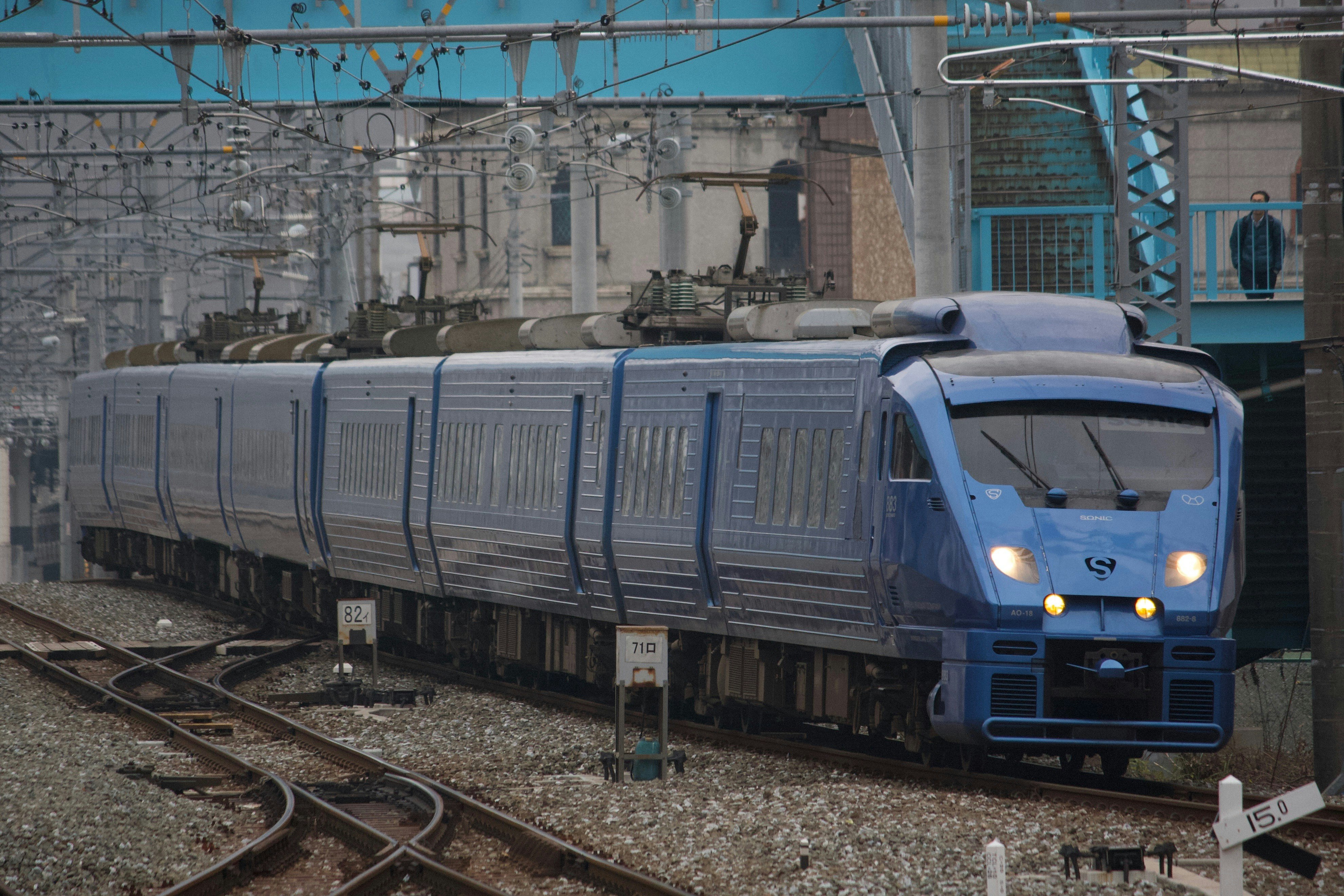 線路を走る青い電車の先頭車両と車両基地の風景