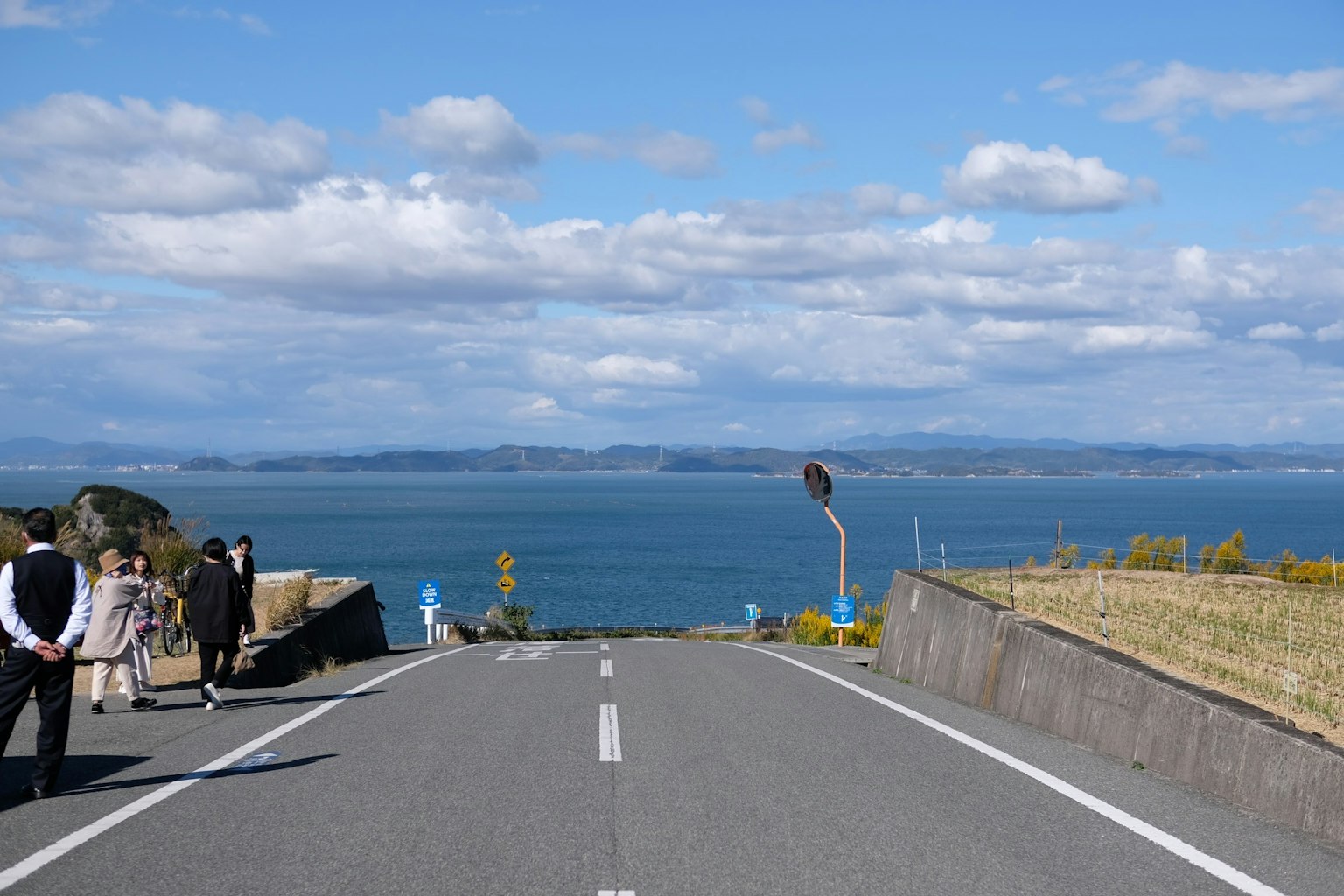 人们步行在道路上，背景是蓝色的海洋和天空