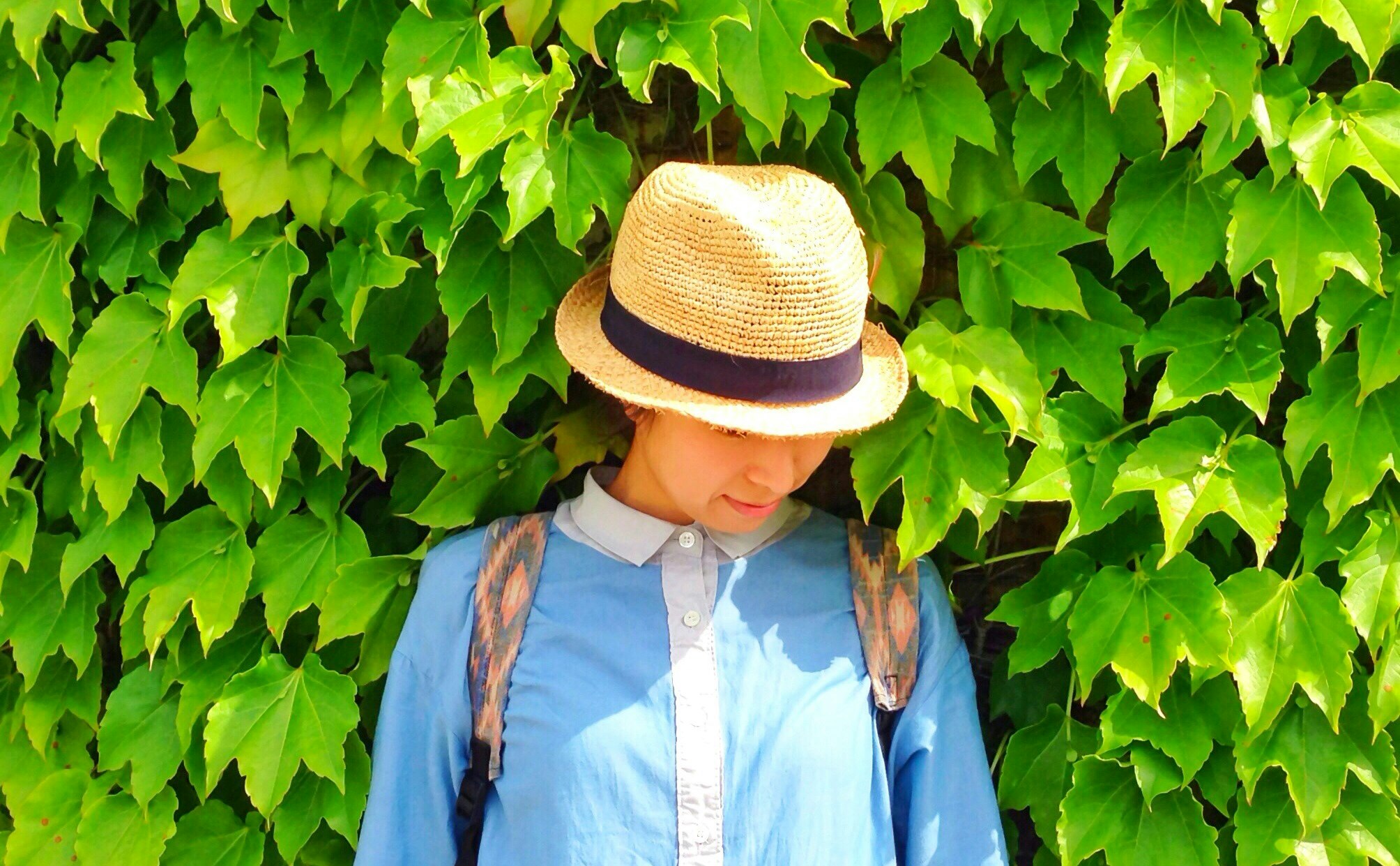 緑の葉に囲まれた麦わら帽子の女性