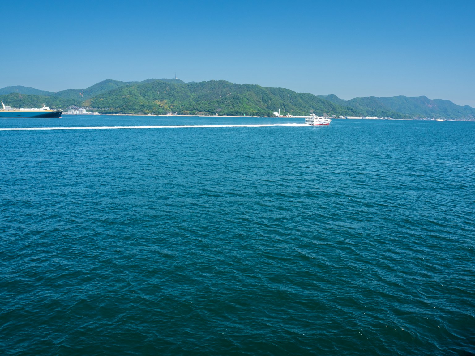 Mar azul claro con montañas verdes al fondo
