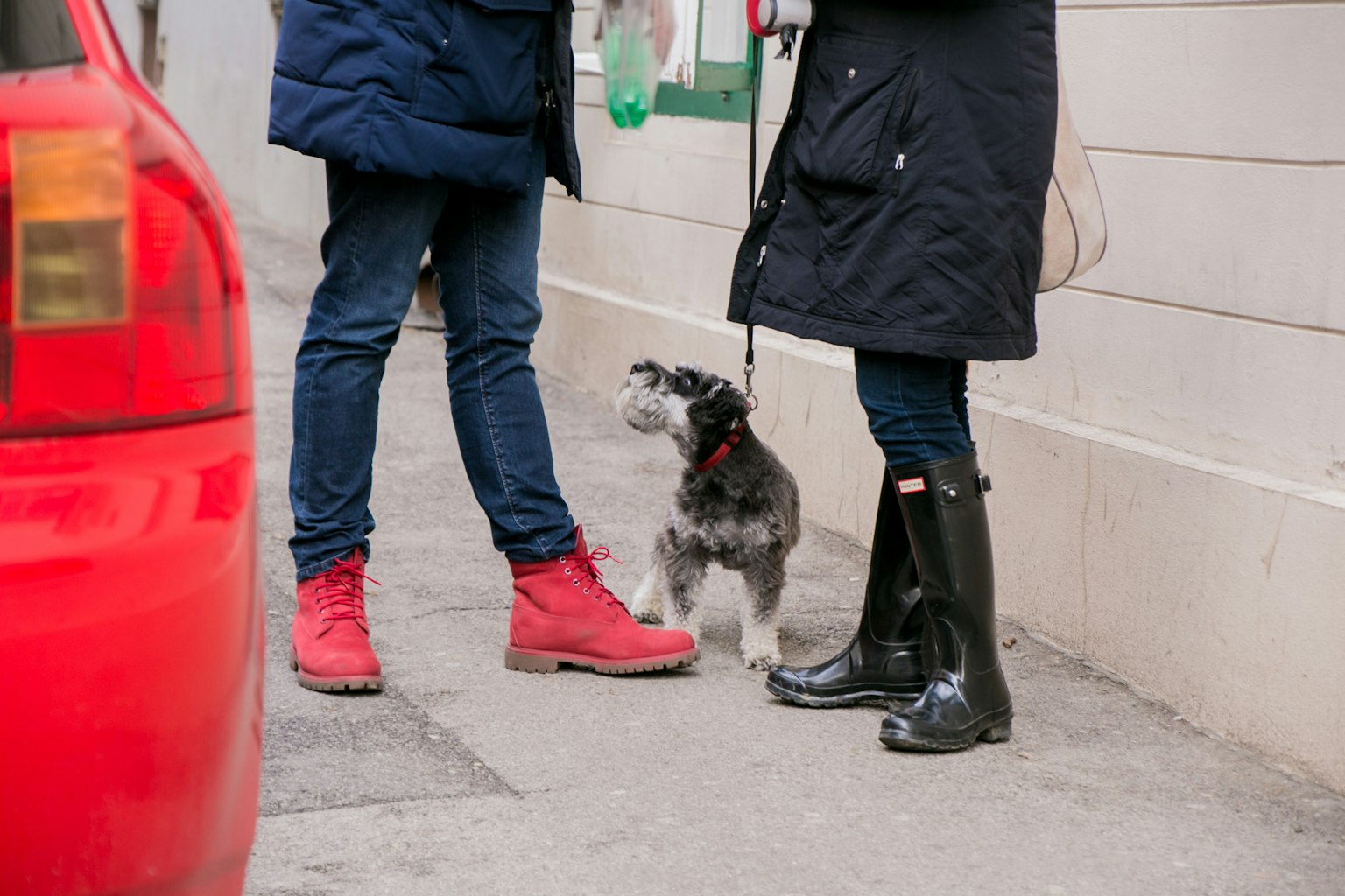 Un homme en bottes rouges et une femme en bottes noires se tenant dans la rue avec un petit chien à leurs pieds