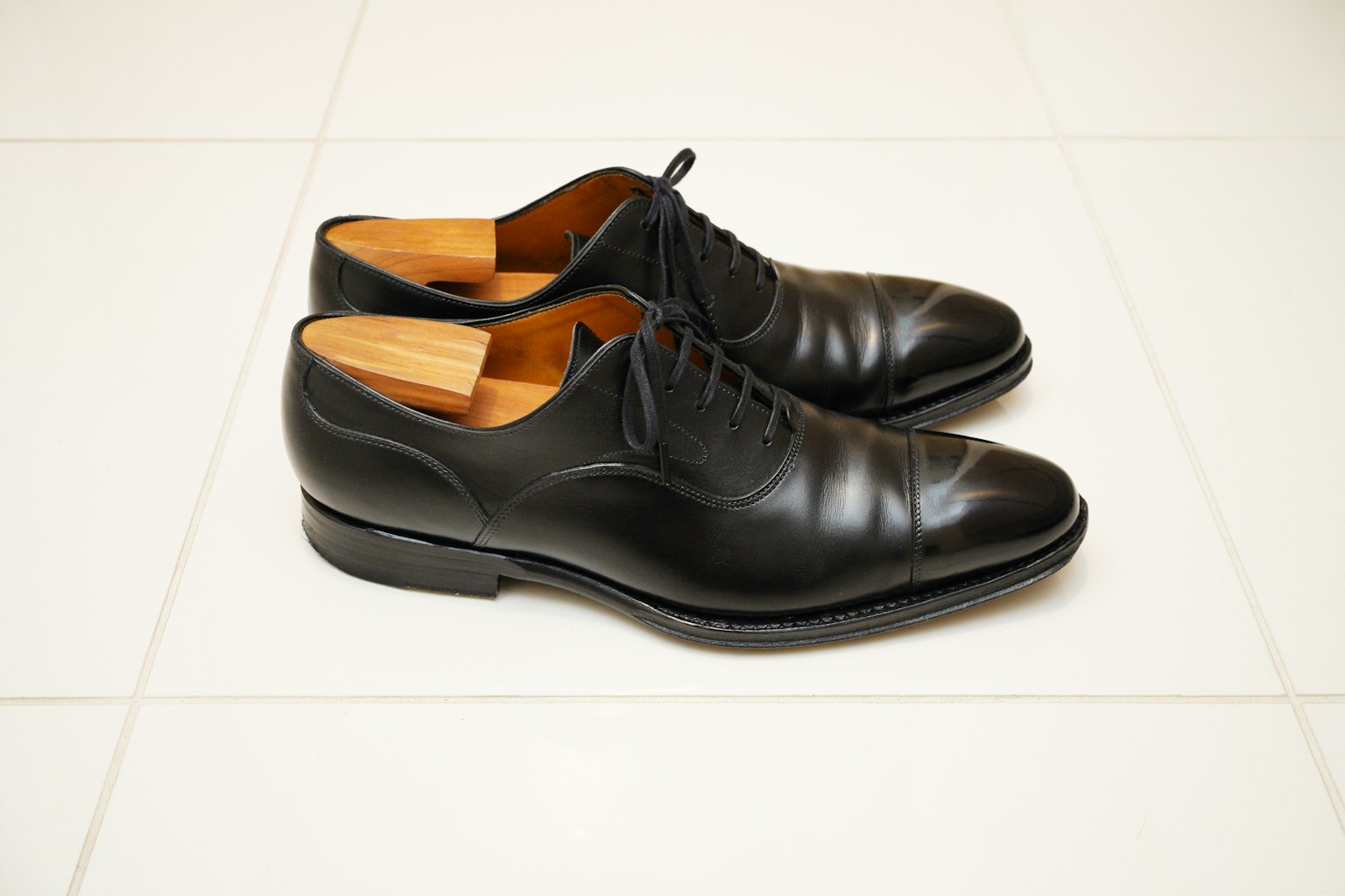 Par de zapatos de cuero negro colocados sobre azulejos blancos