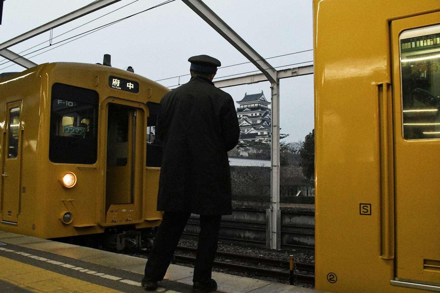 Scena di stazione con un lavoratore in attesa accanto a un treno giallo