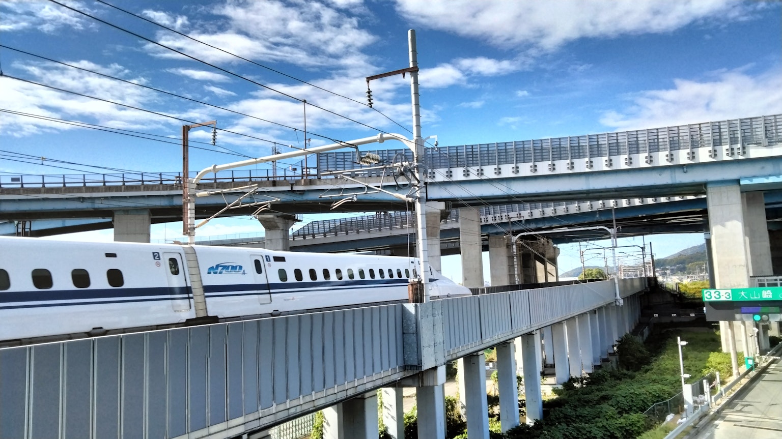 Shinkansen-Zug fährt unter einer erhöhten Struktur mit blauem Himmel