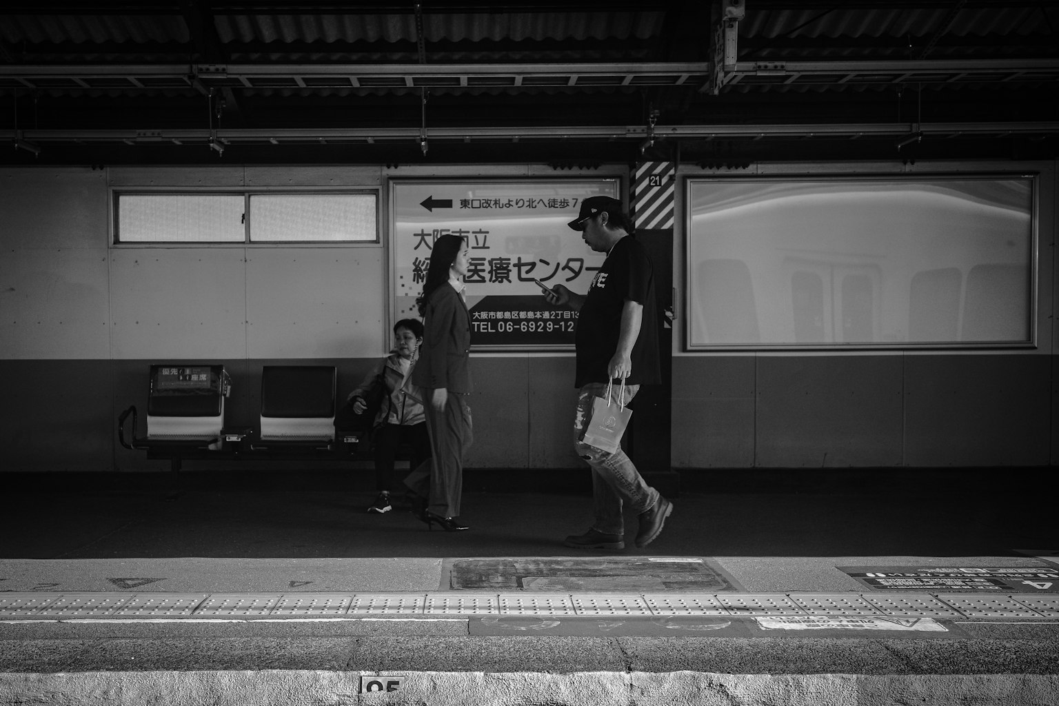 Photo en noir et blanc de personnes marchant sur un quai de train avec une personne assise