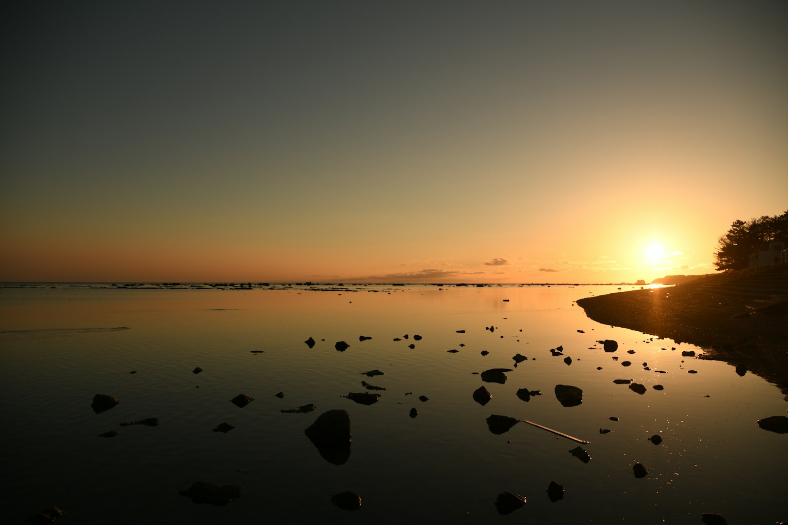 Calm shoreline with a sunset reflecting on a tranquil water surface