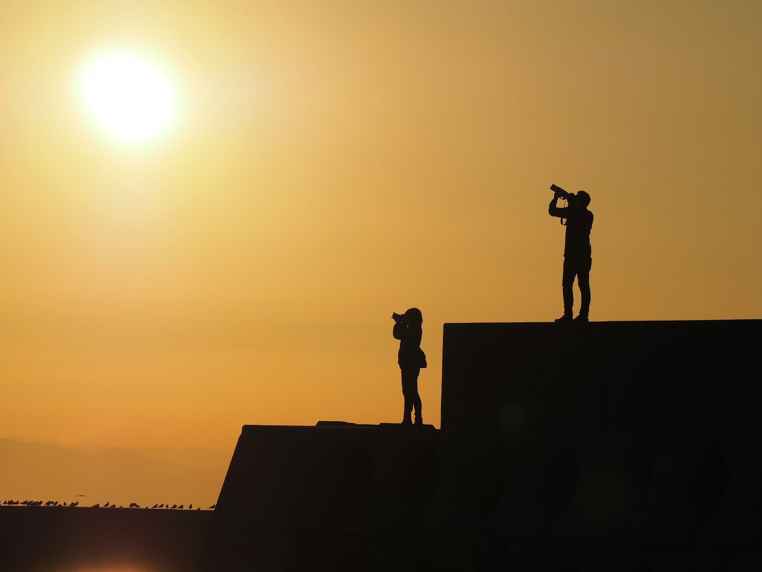 Silhouettes of two people holding cameras against a sunset