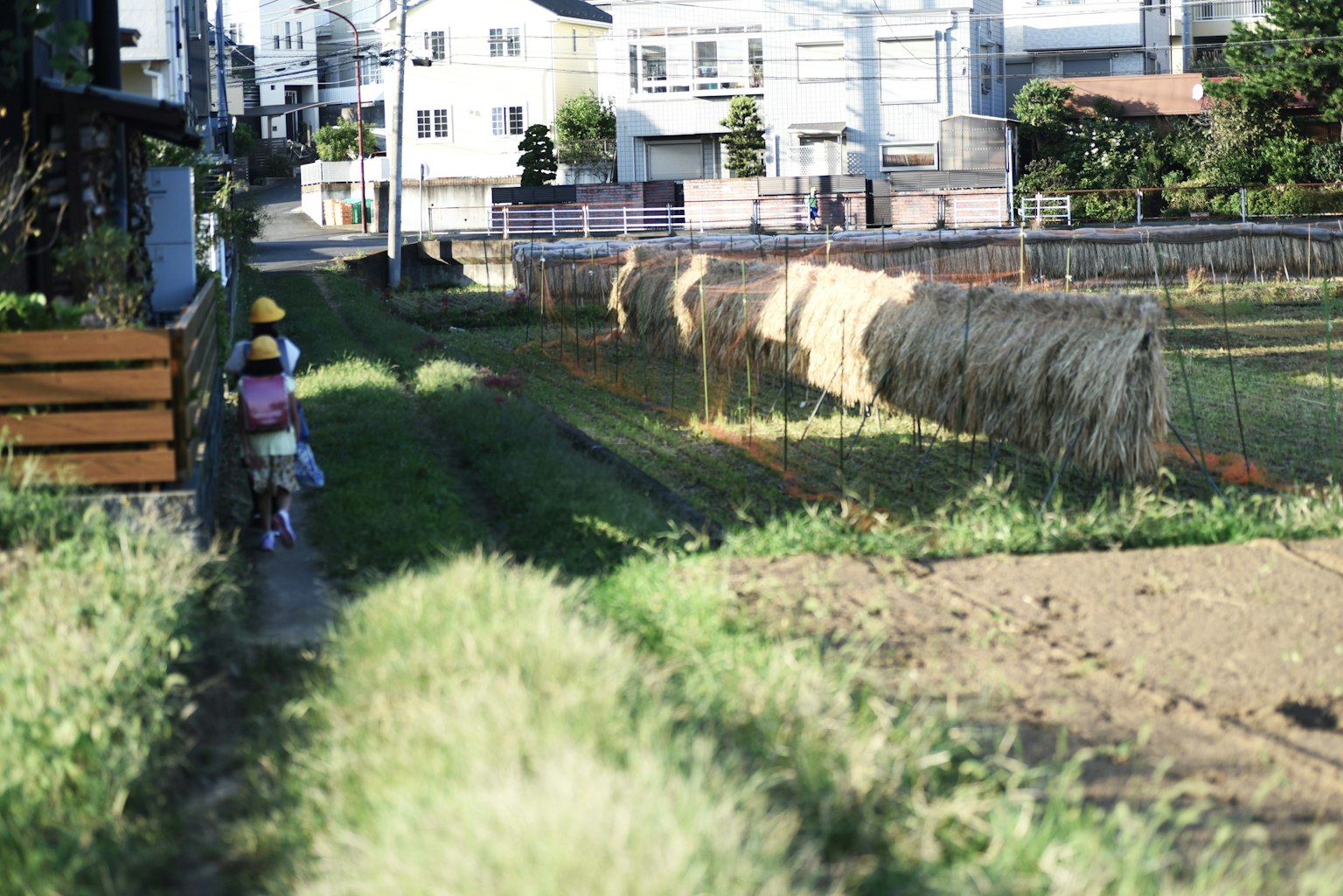 A child walking along a rural path with houses and hay bales in the background