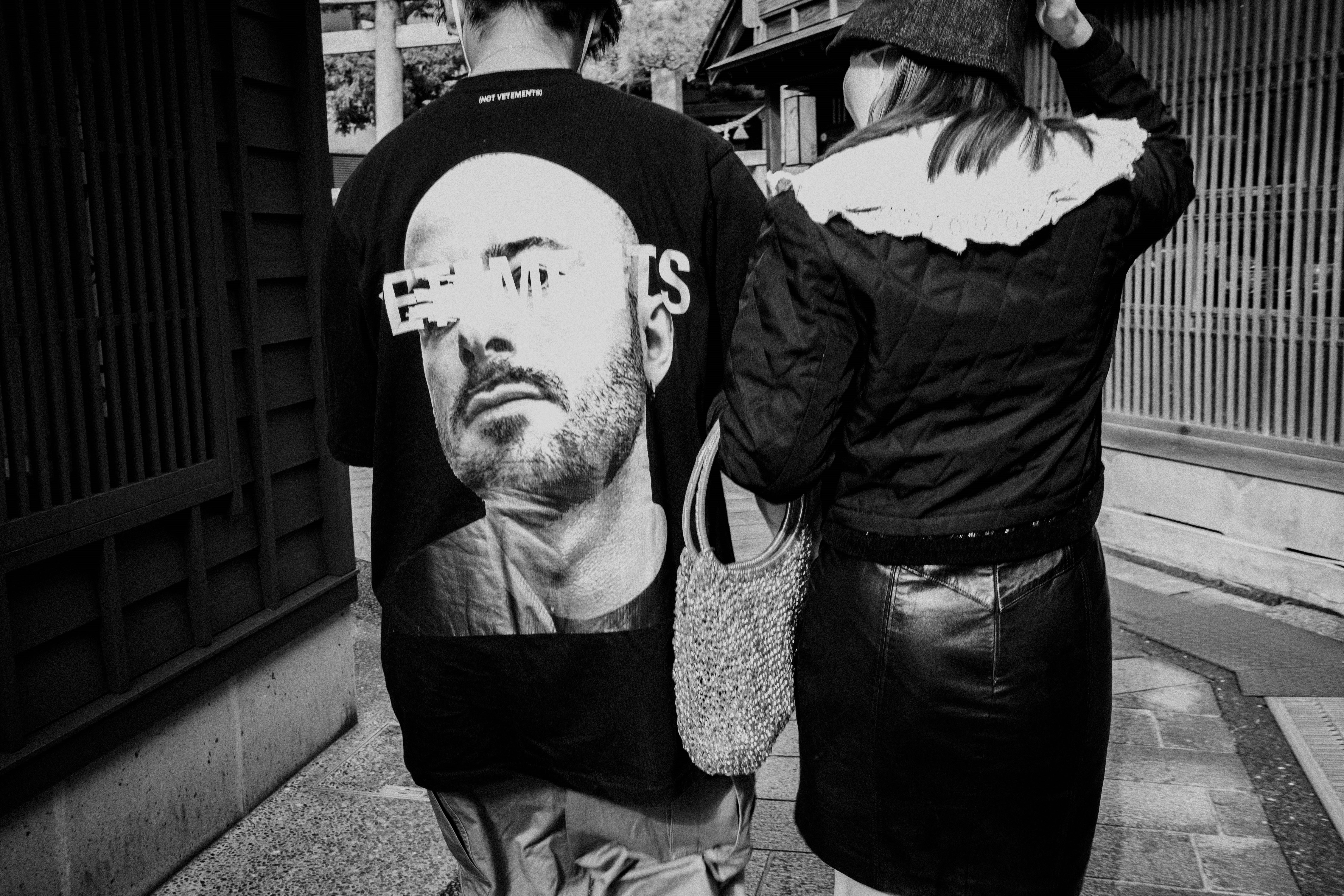 路地の壁に貼られた人物ポートレートTシャツと手に持つ袋