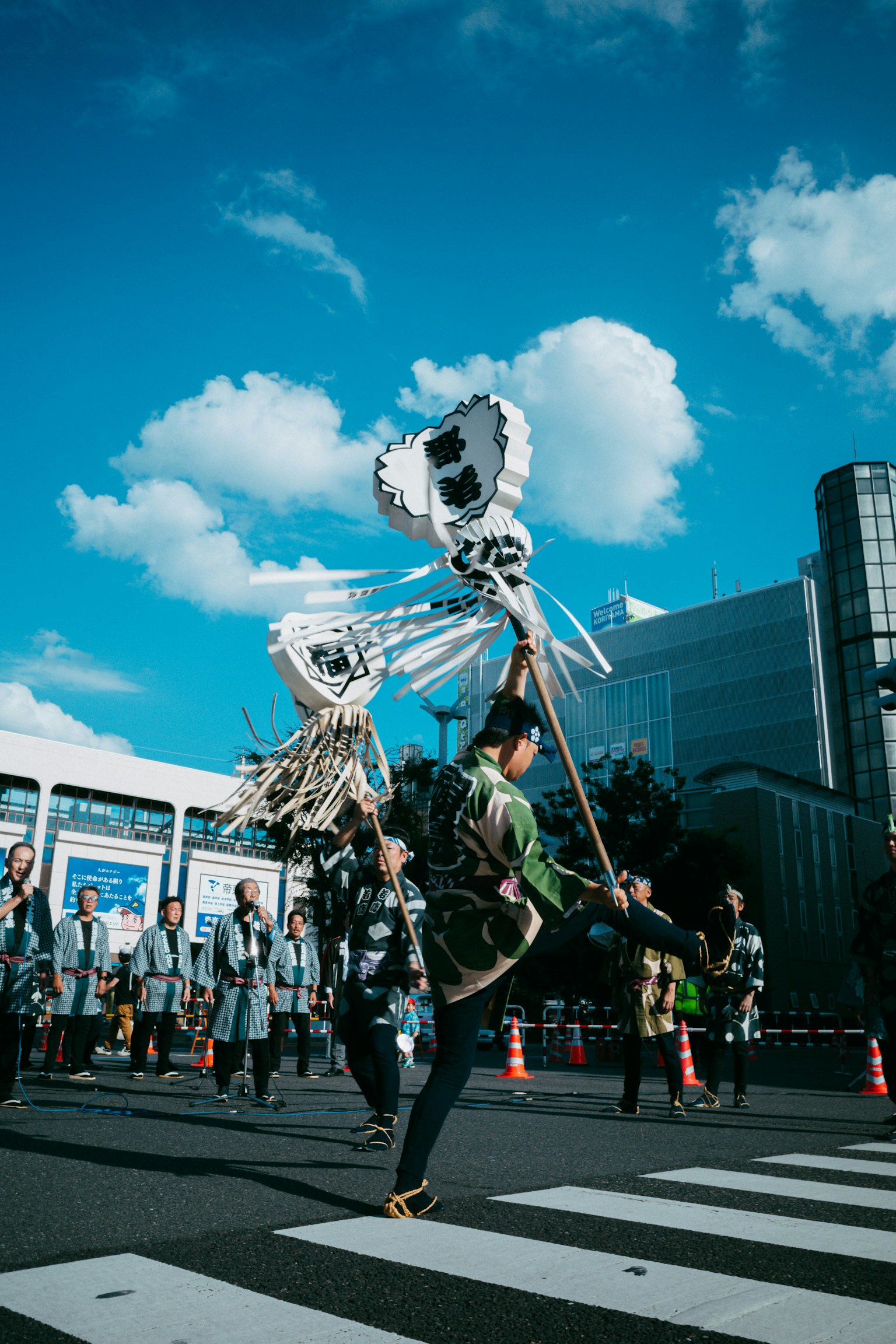 A person in festival attire dancing while holding a traditional instrument in an urban setting