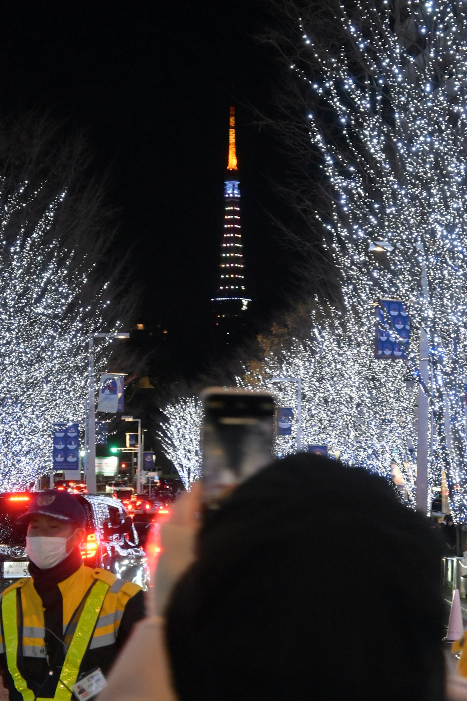 Una persona che cattura la torre di Tokyo illuminata in una strada fiancheggiata da luci scintillanti