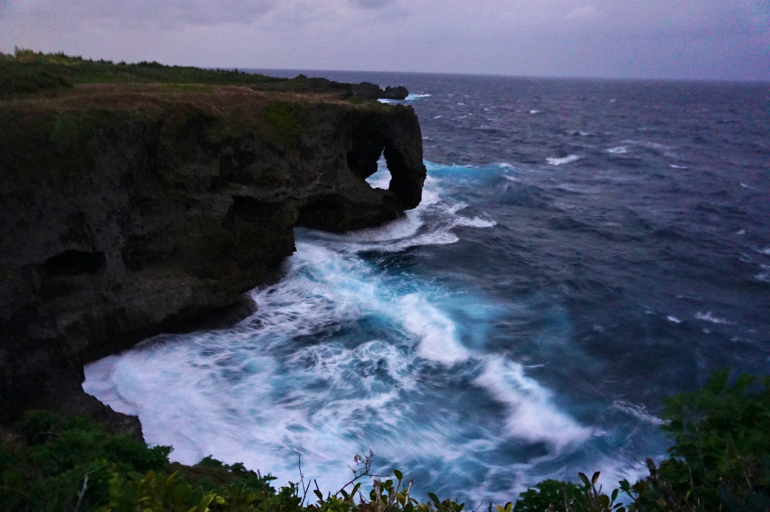 Lengkungan batu menghadap laut dengan ombak yang menghantam