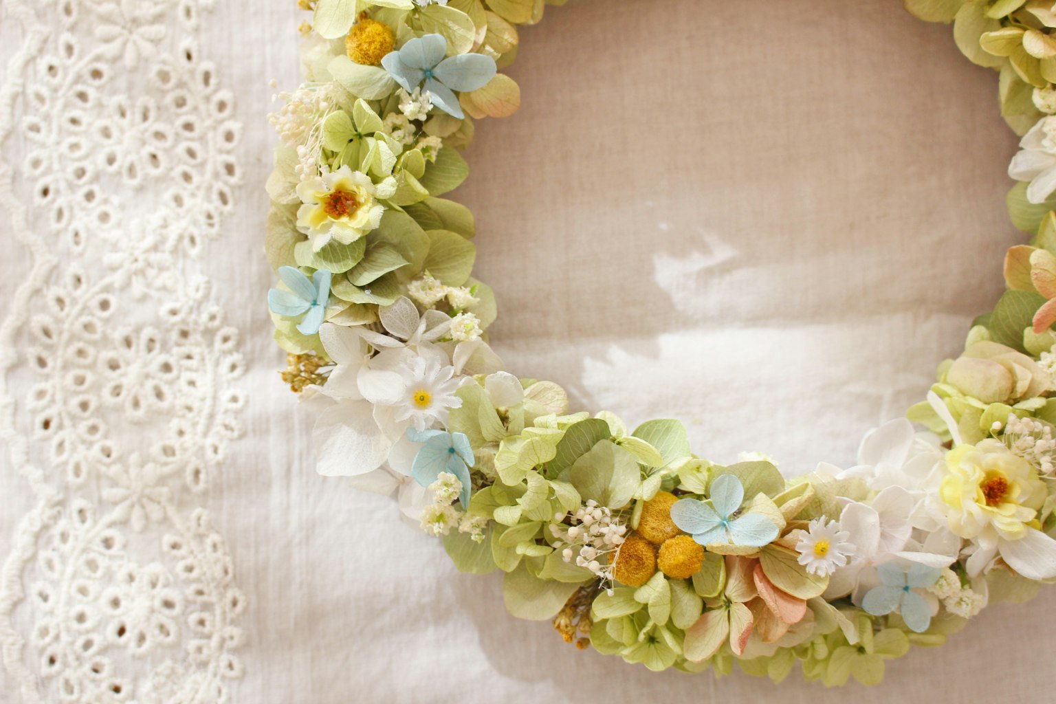 Ein grüner Kranz mit pastellfarbenen Blumen auf einem weißen Stoff
